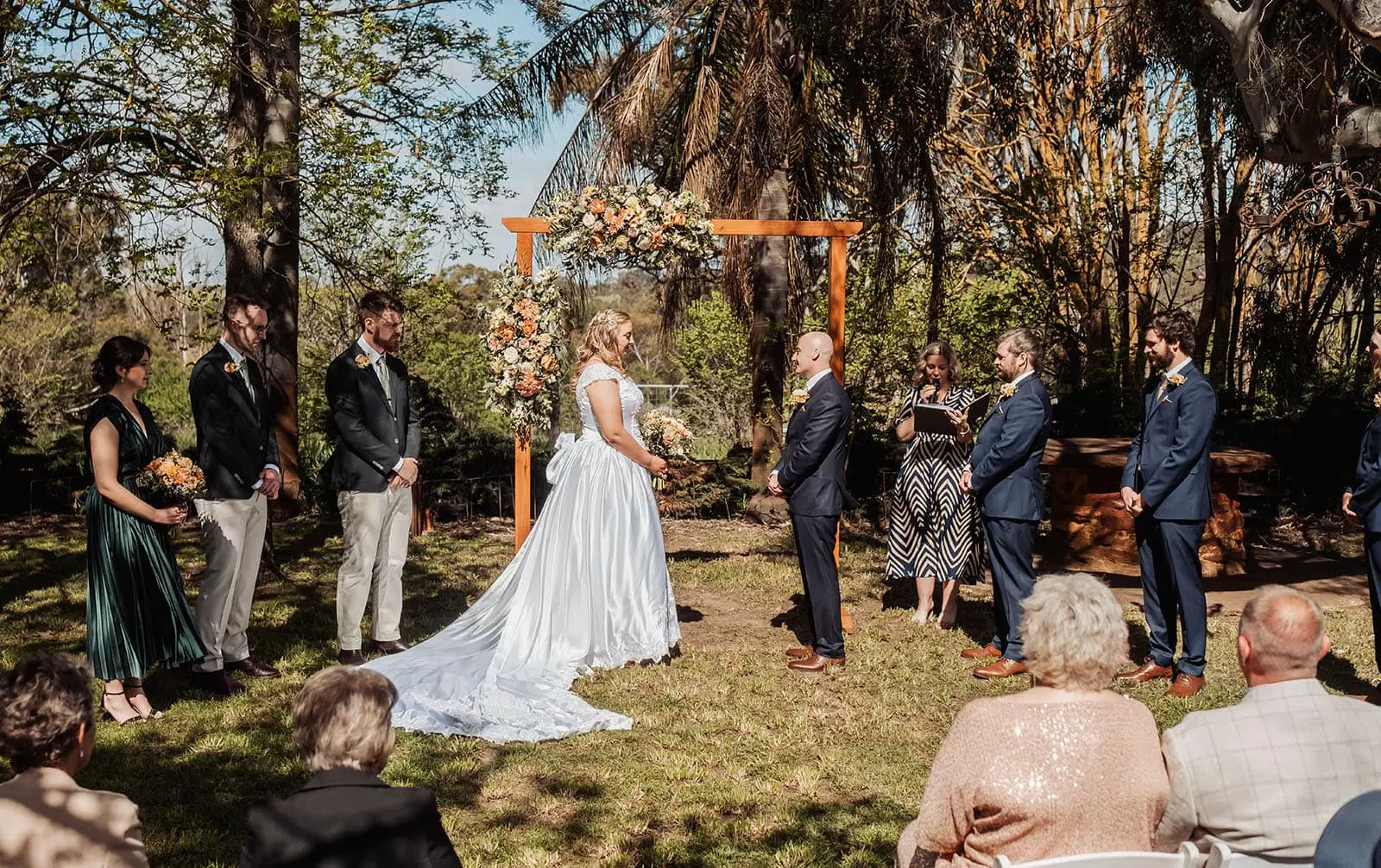 grand cru estate wedding - isabella & nick 124 Elegant outdoor wedding ceremony with floral decorations under sunny skies.