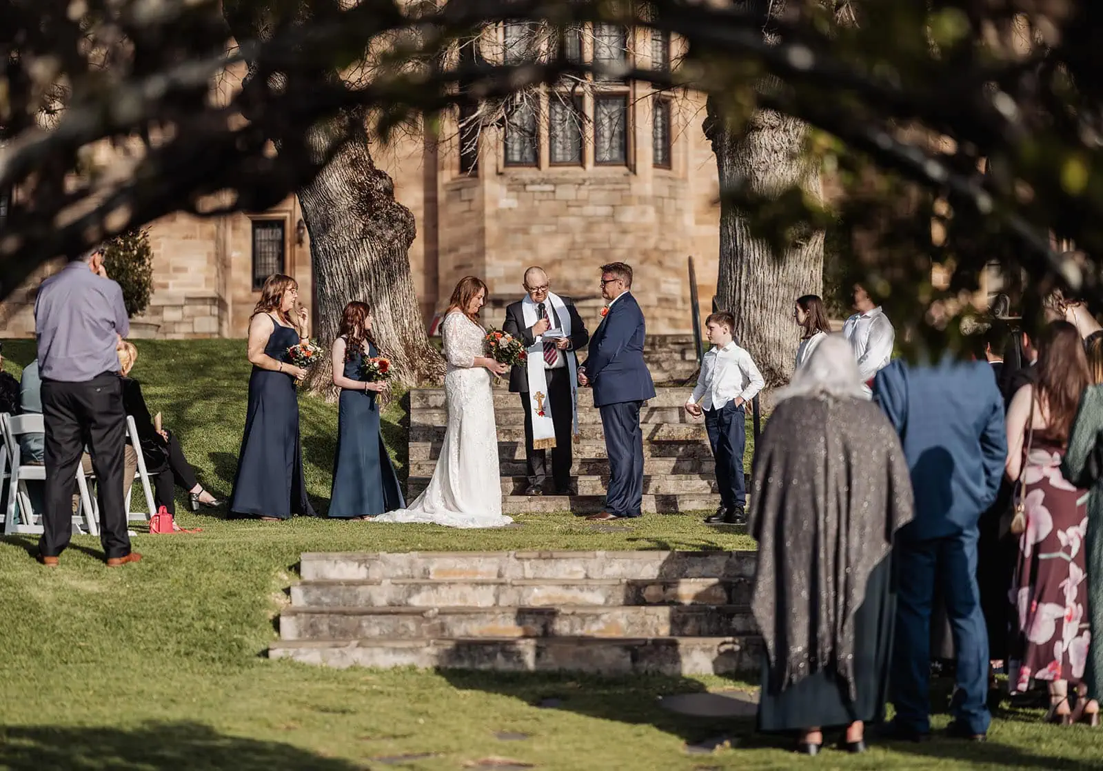 carrick hill wedding - jo & david 292 Outdoor wedding ceremony with floral decorations under a sunny sky.
