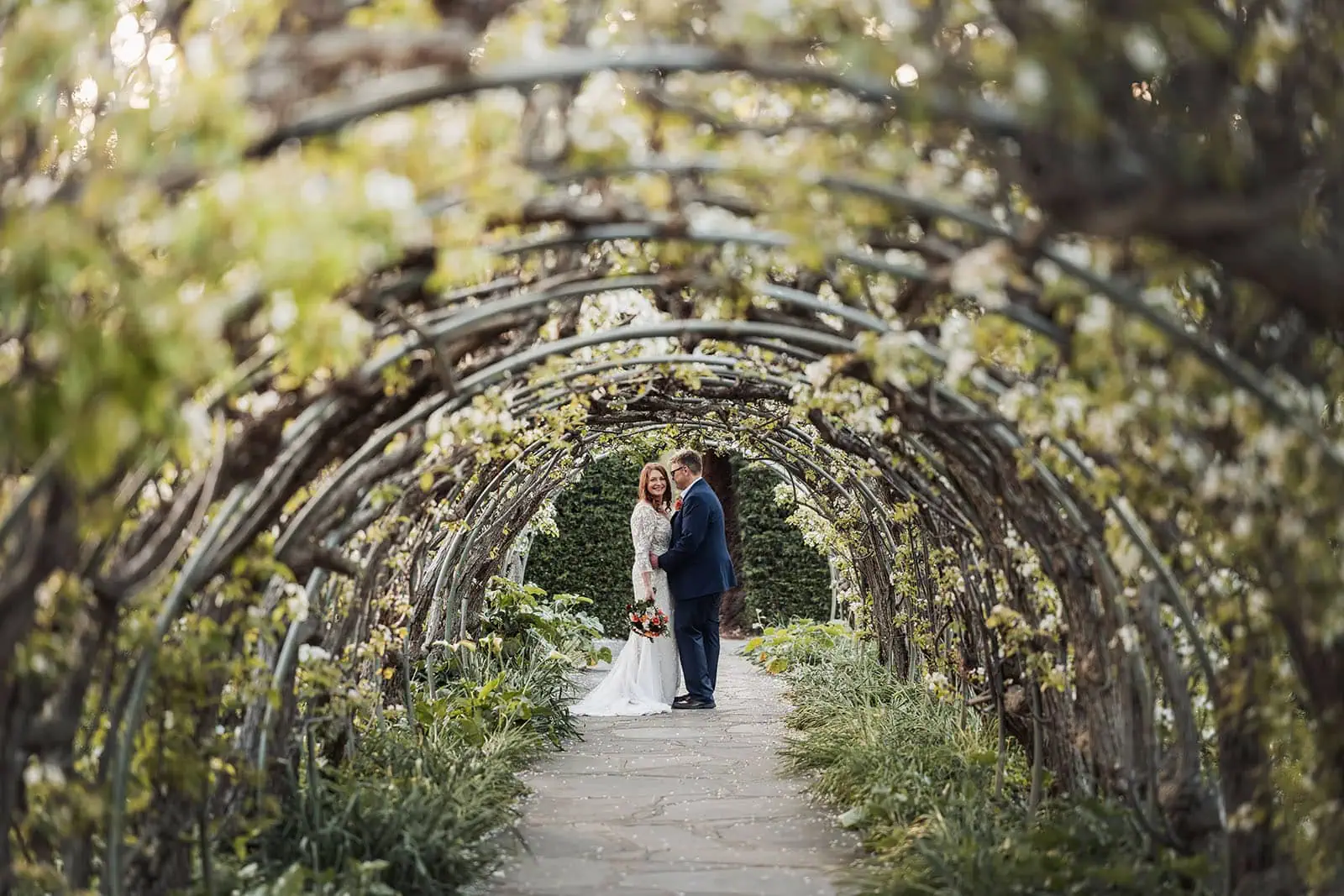 carrick hill wedding - jo & david 306 Couple embracing under a romantic archway at sunset.