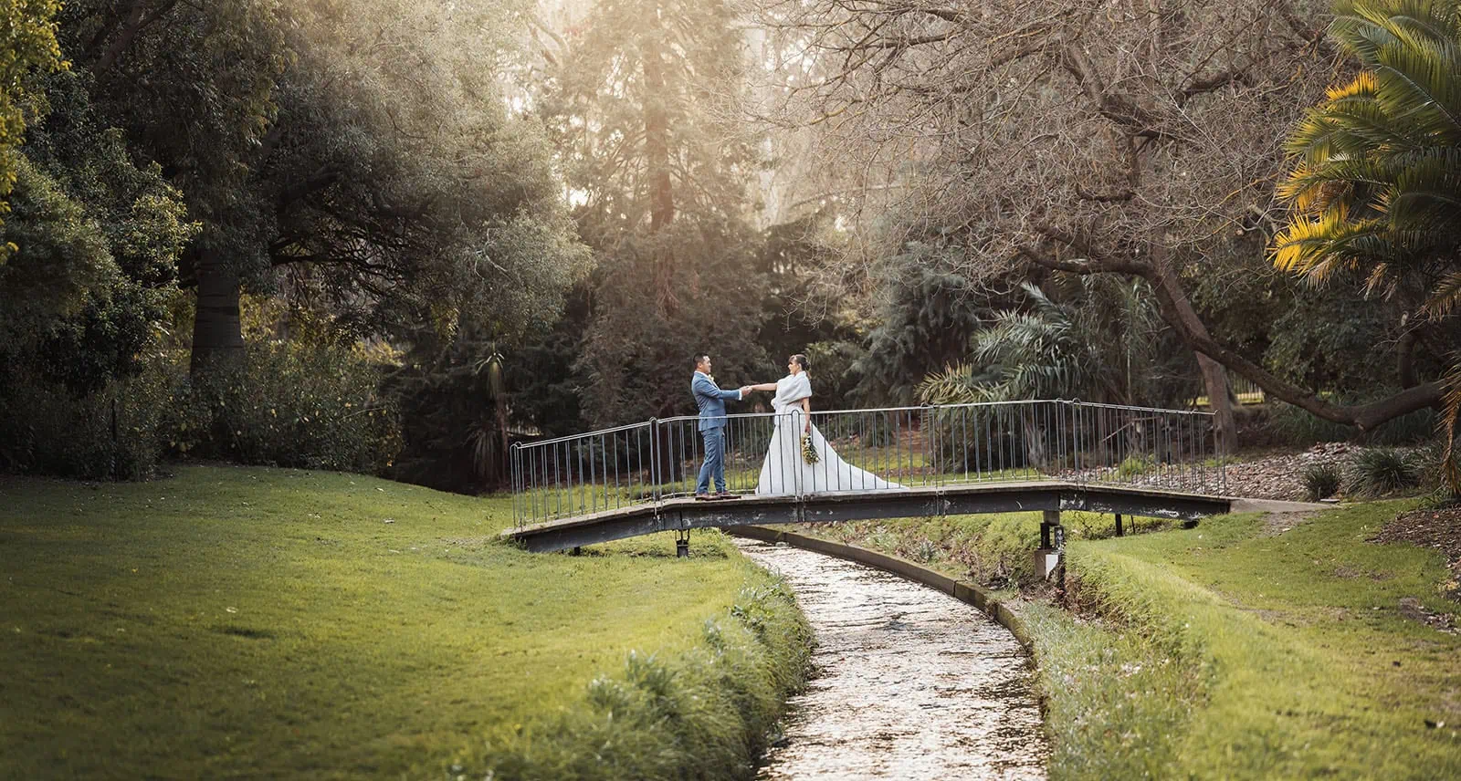 adelaide botanic gardens summerhouse wedding - belinda & ian 189 Couple enjoying a peaceful moment on a scenic bridge at sunset.