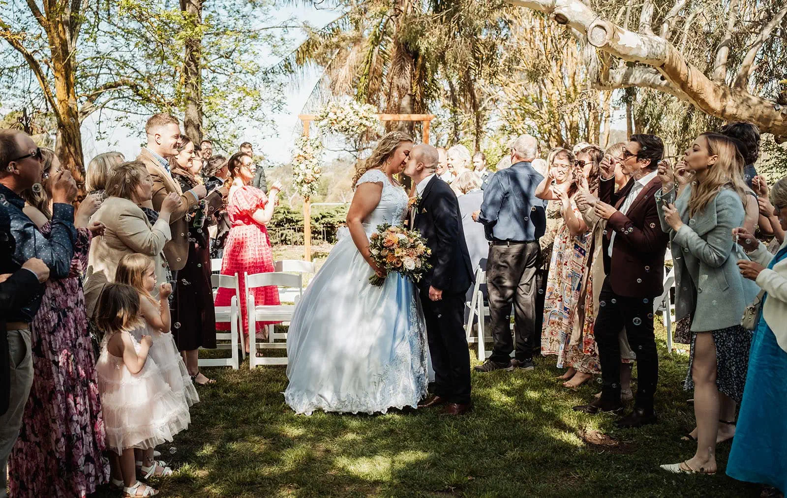 grand cru estate wedding - isabella & nick 129 Outdoor wedding ceremony with elegant floral decorations and guests seated under clear skies.