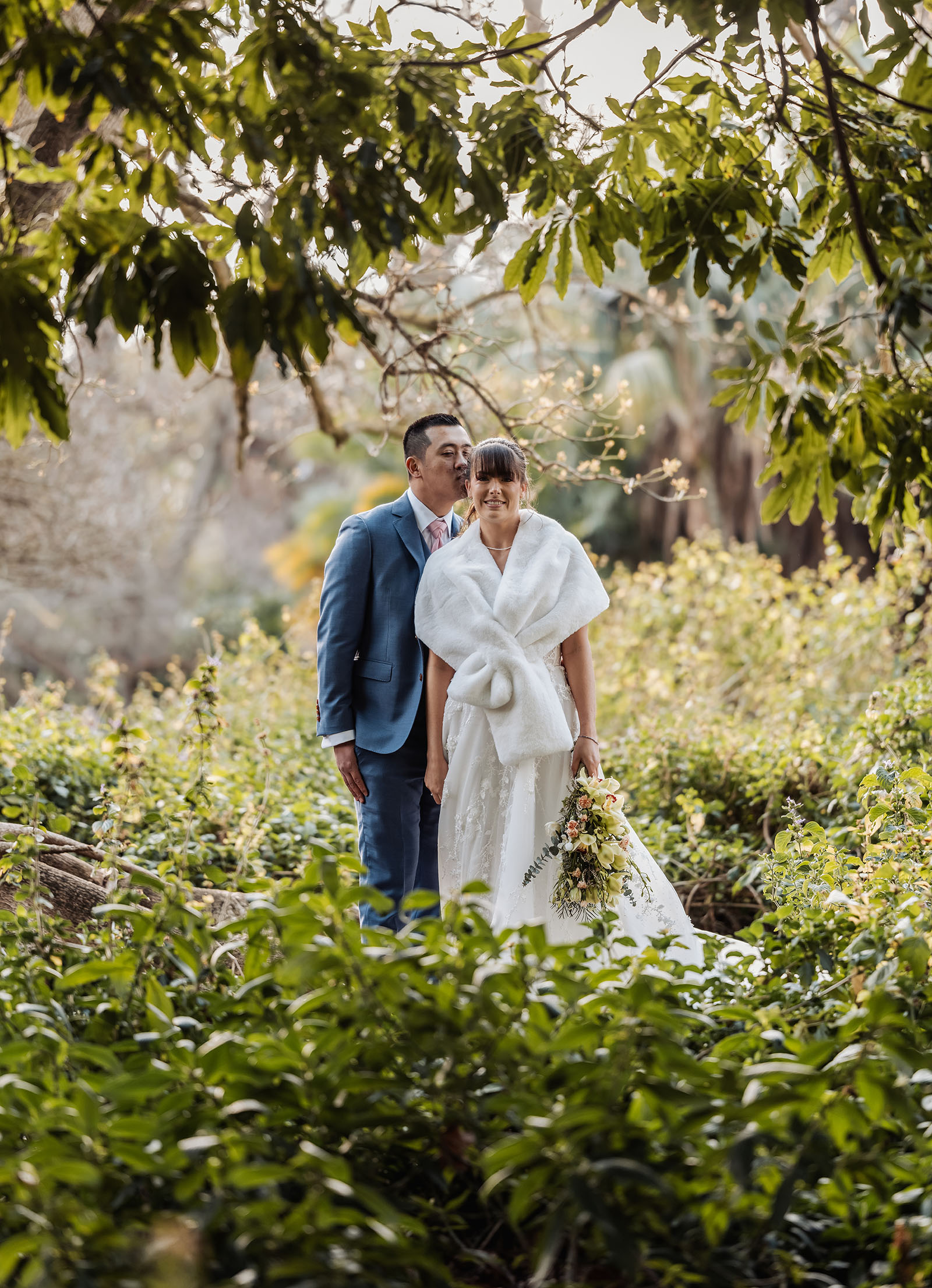 adelaide botanic gardens summerhouse wedding - belinda & ian 187 Bride and groom embrace in lush garden wedding scene.