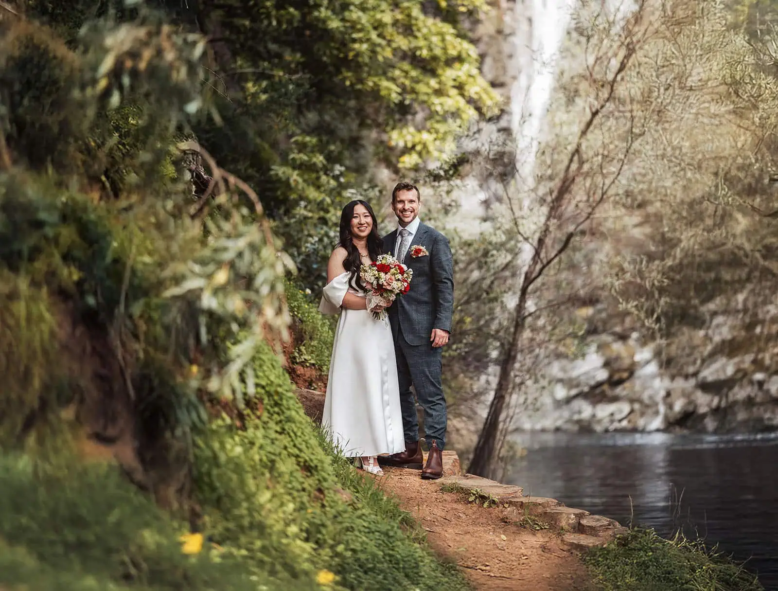 utopia waterfall gully wedding - sally & ben 249 Bride and groom walking on scenic forest path during outdoor wedding ceremony.