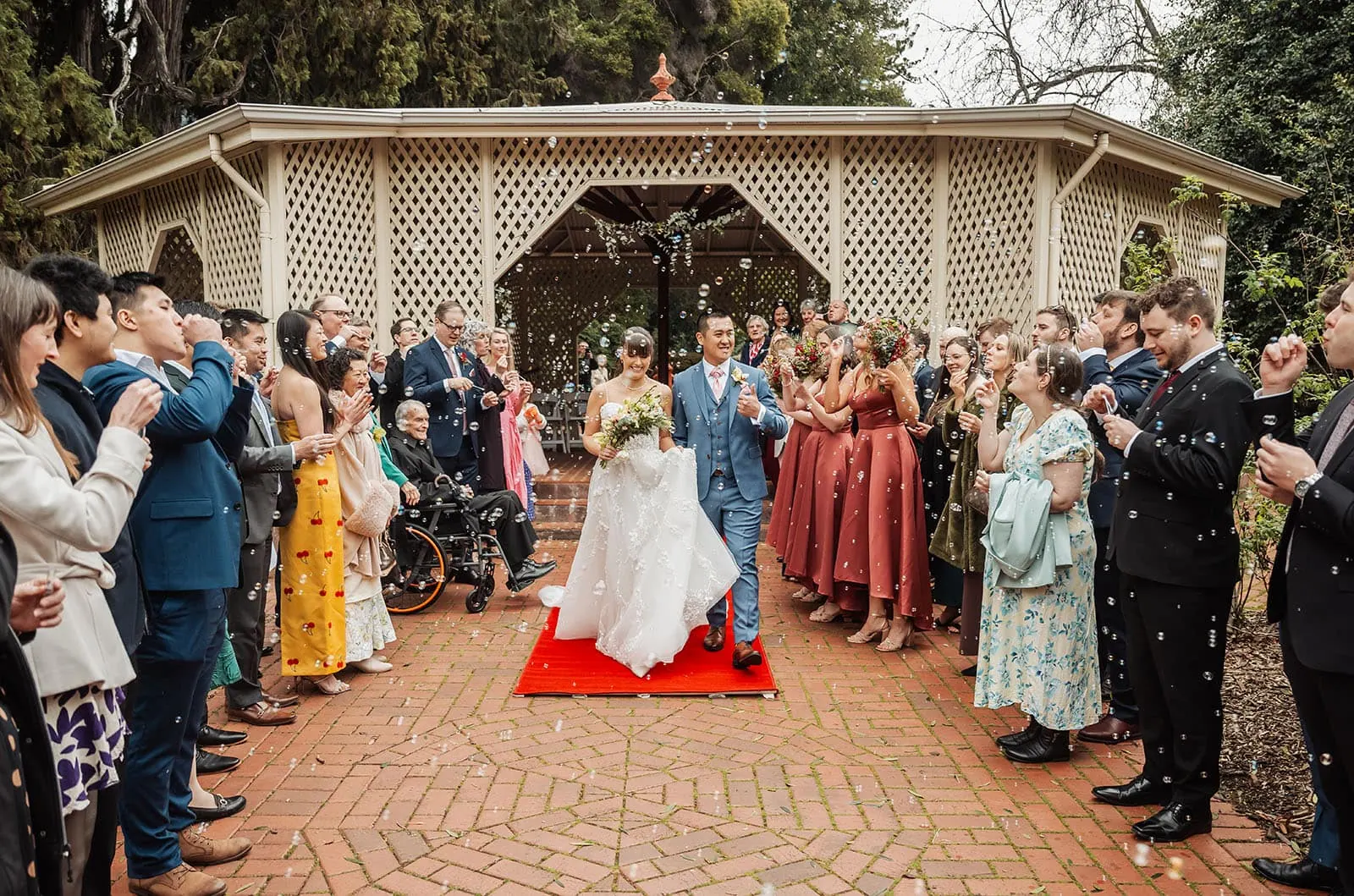 adelaide botanic gardens summerhouse wedding - belinda & ian 170 Bride and groom surrounded by joyful wedding guests blowing bubbles.