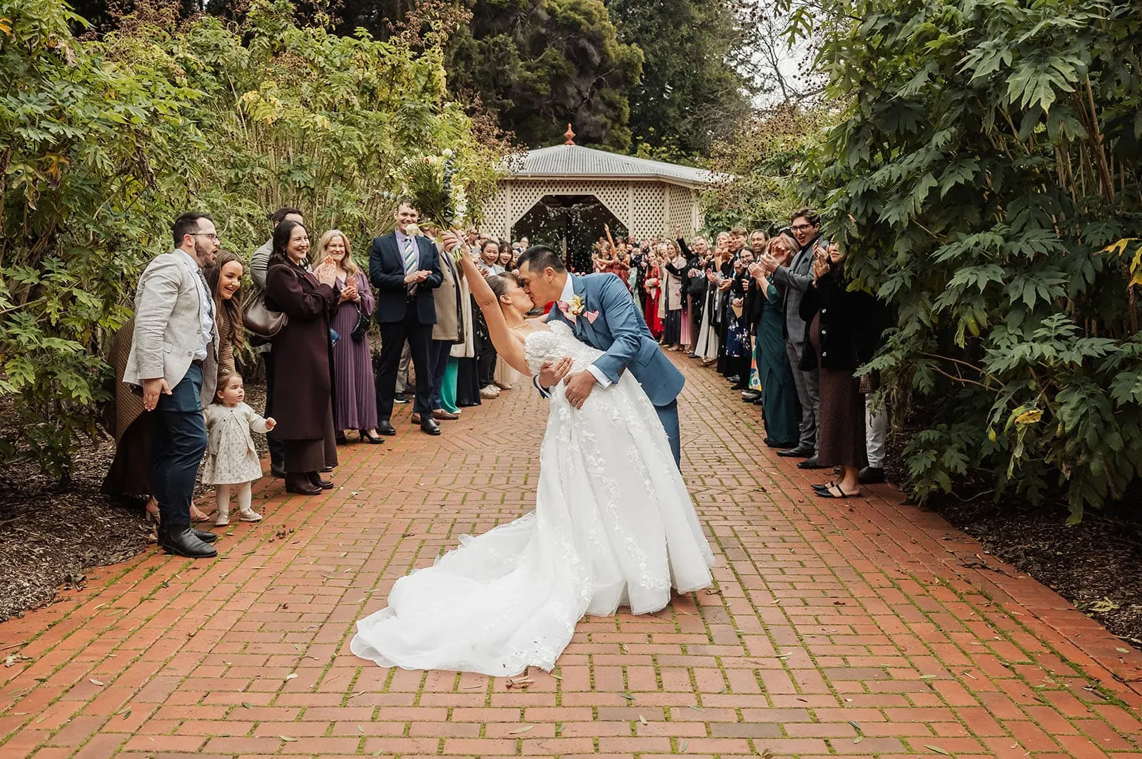 adelaide botanic gardens summerhouse wedding - belinda & ian 171 Wedding couple kissing on a brick pathway surrounded by greenery.