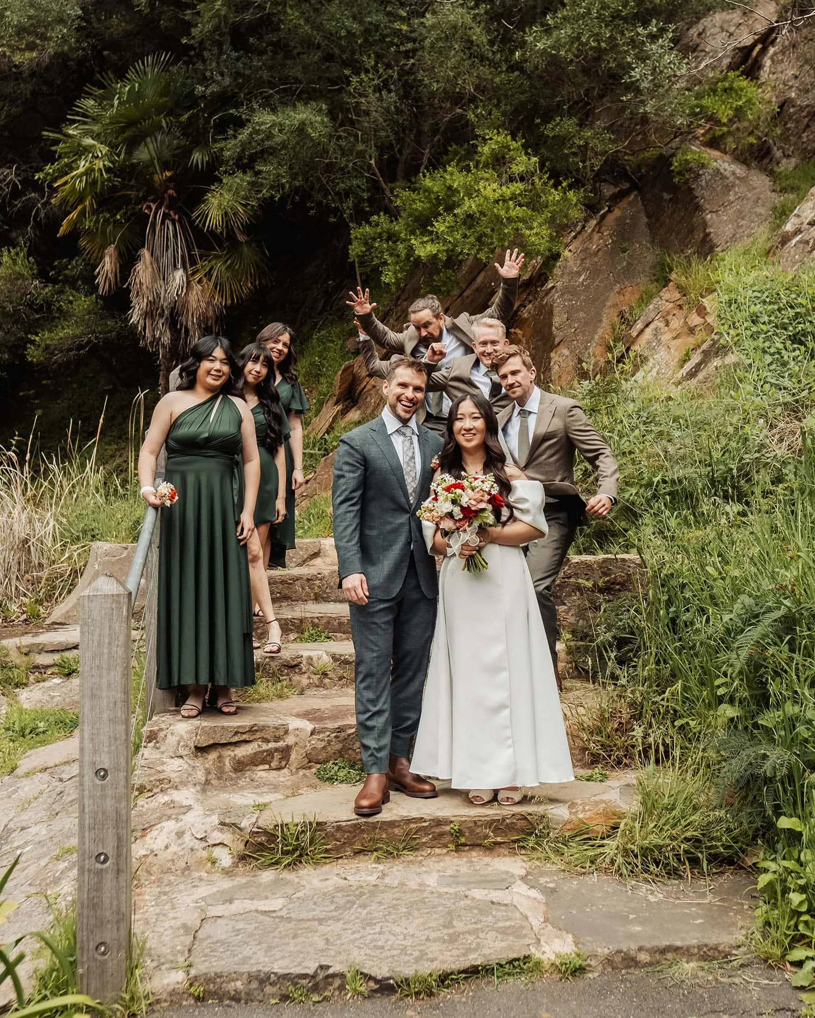 utopia waterfall gully wedding - sally & ben 238 Bride and groom with wedding party on stairs, elegant celebration setting.