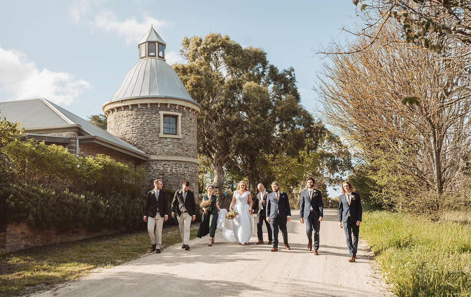 grand cru estate wedding - isabella & nick 138 Bride and groom walking with bridesmaids and groomsmen in a picturesque garden setting.