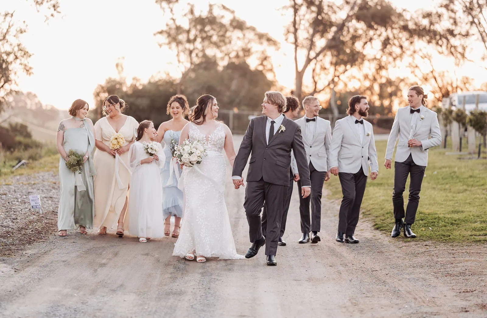 beach rd wines wedding - hana & jessie 82 Wedding party walking on sunset-lit path, celebrating love and unity.