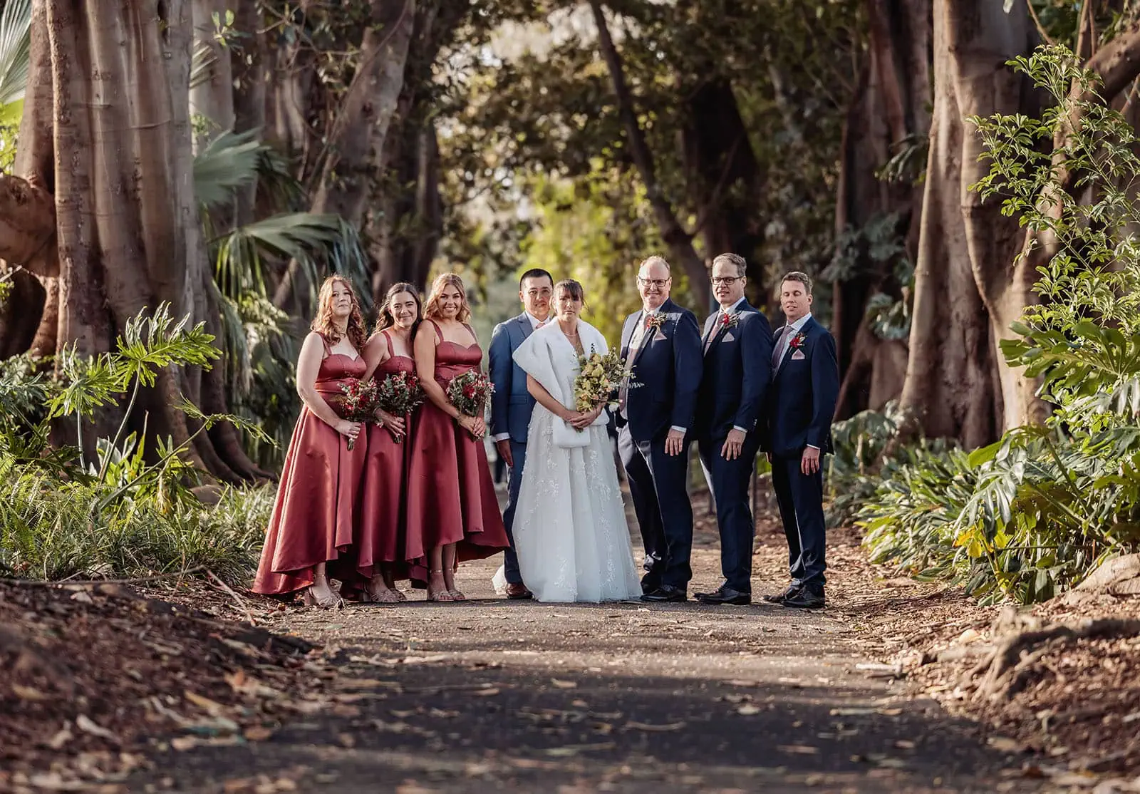 adelaide botanic gardens summerhouse wedding - belinda & ian 186 Wedding party walking down a scenic tree-lined path, celebrating love outdoors.