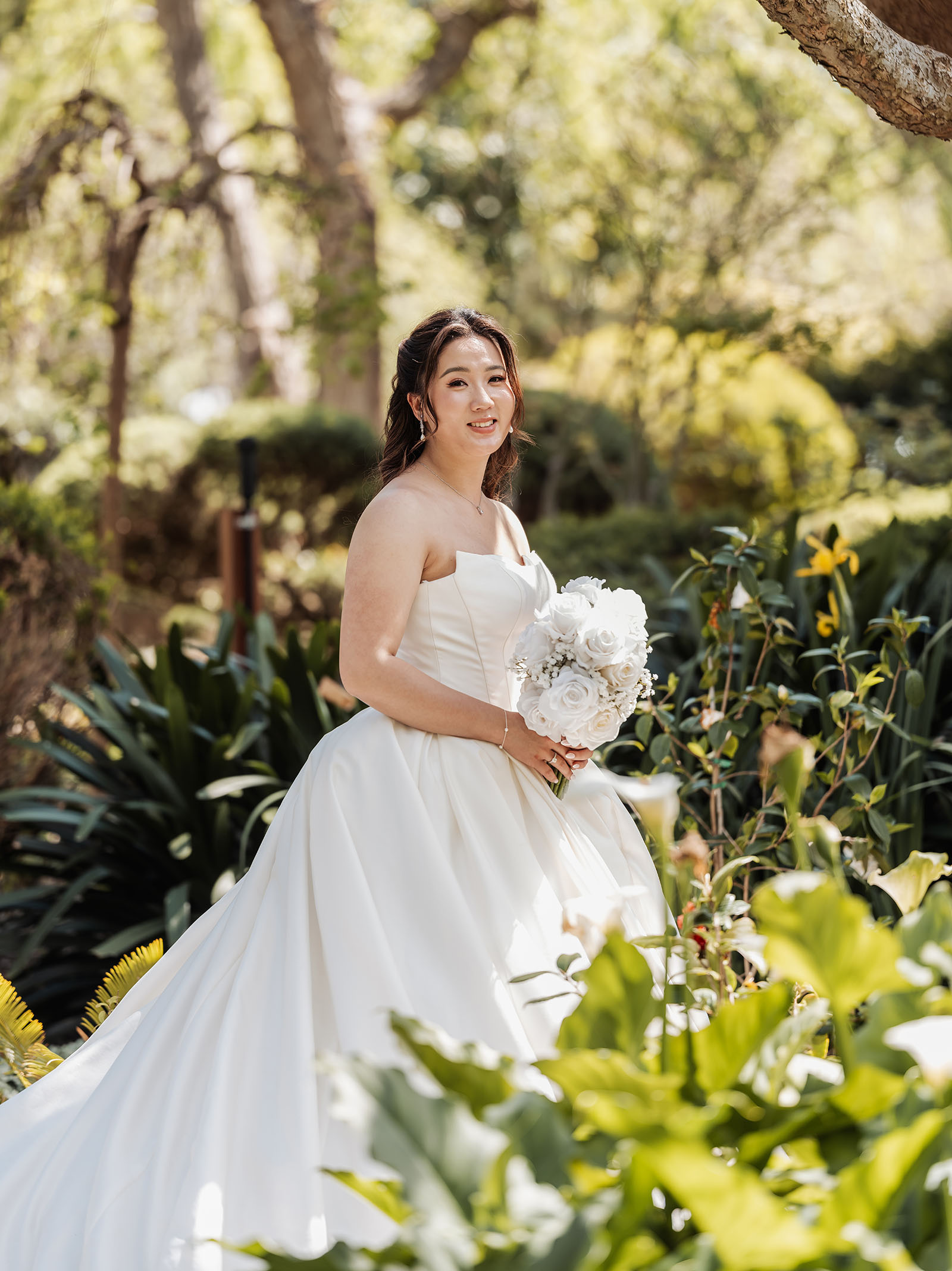 sunnybrae rose garden wedding - celina & anuj 34 Bride standing in sunlit garden, surrounded by flowers and greenery.
