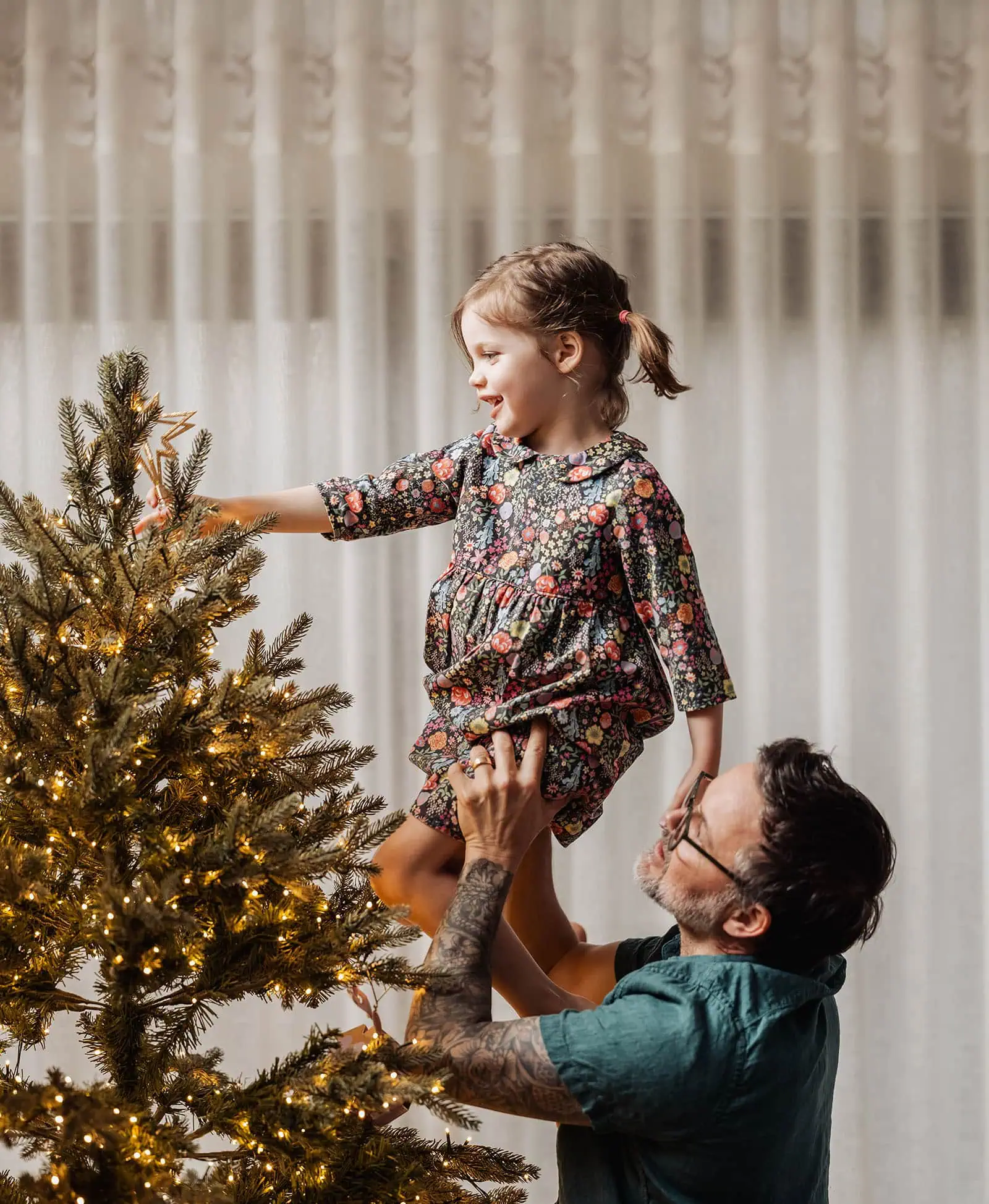 goodwood family photoshoot 110 Father and daughter decorating Christmas tree with ornaments and lights.