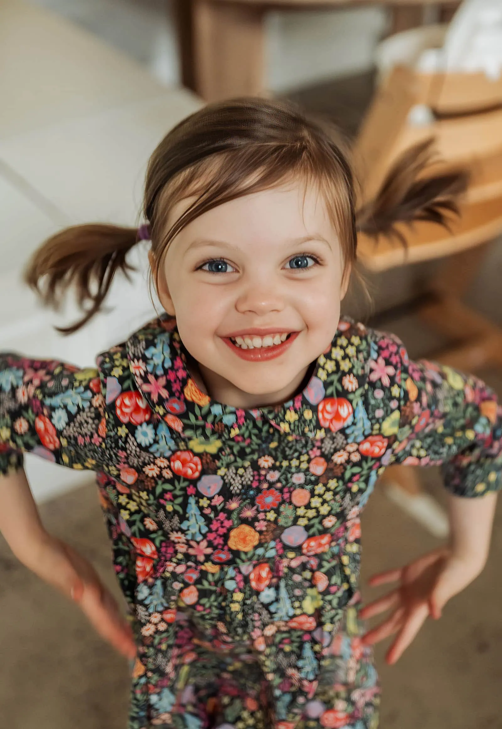 goodwood family photoshoot 103 Young girl smiling in a colorful floral dress outdoors.