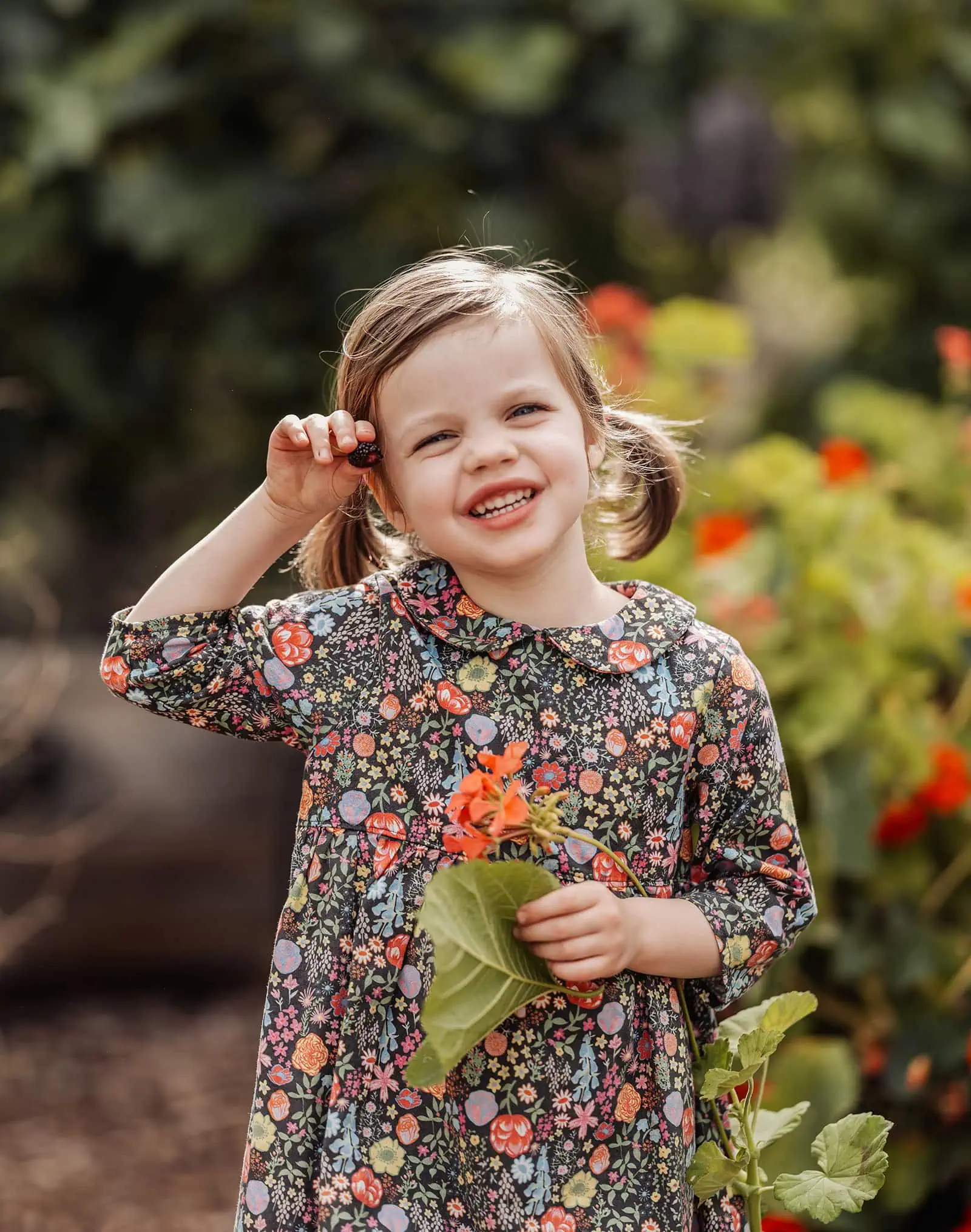 goodwood family photoshoot 126 Joyful young girl smiling in vibrant garden filled with flowers.