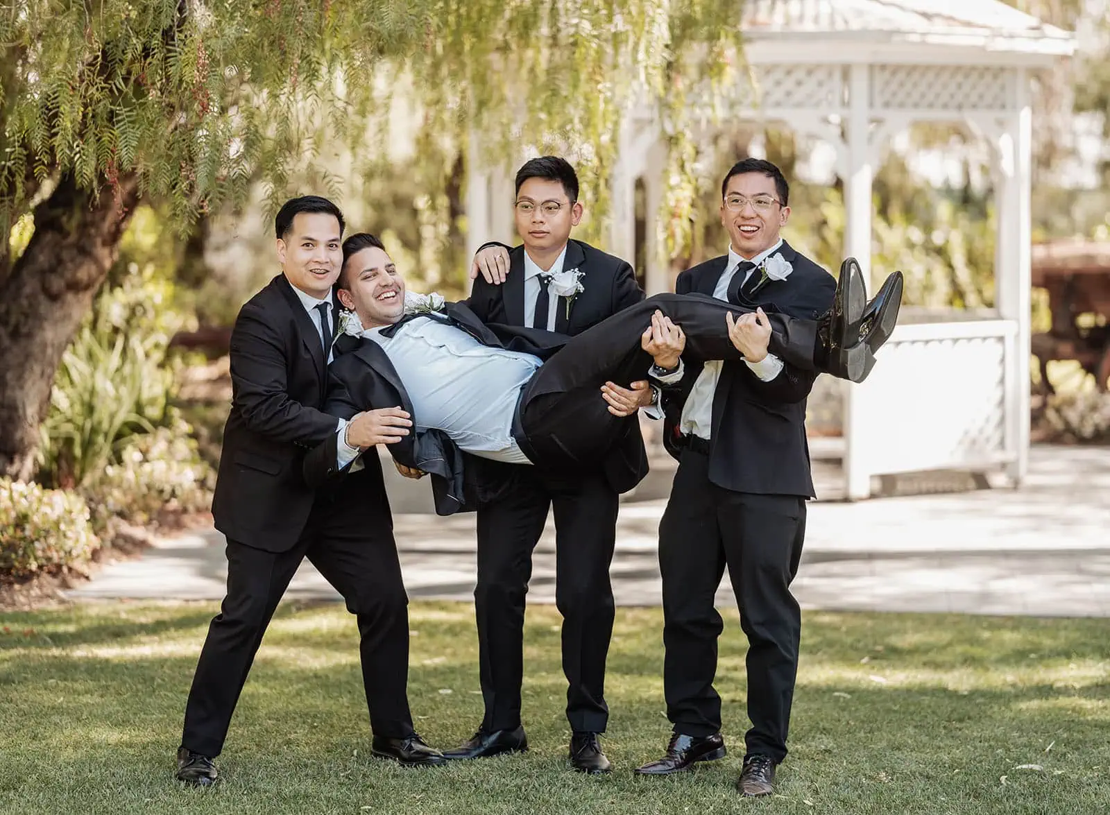 sunnybrae rose garden wedding - celina & anuj 57 Men carrying a person in a garden setting.