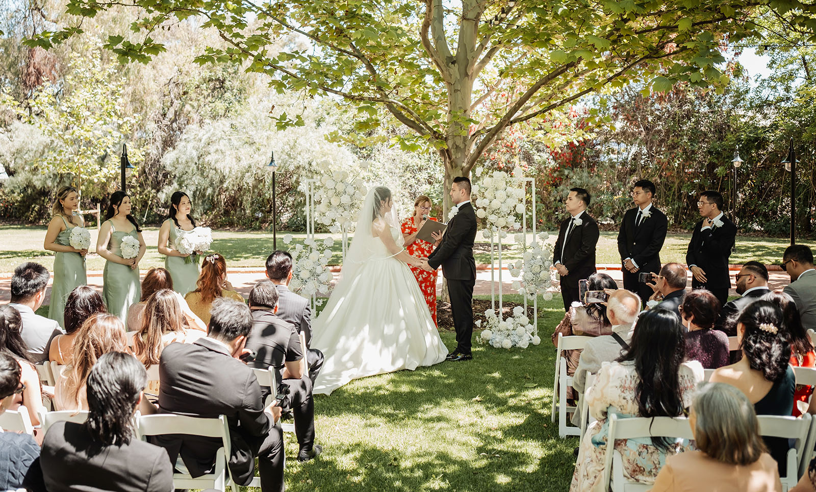 sunnybrae rose garden wedding - celina & anuj 48 Elegant outdoor wedding ceremony with floral decorations and guests seated under a sunny sky.