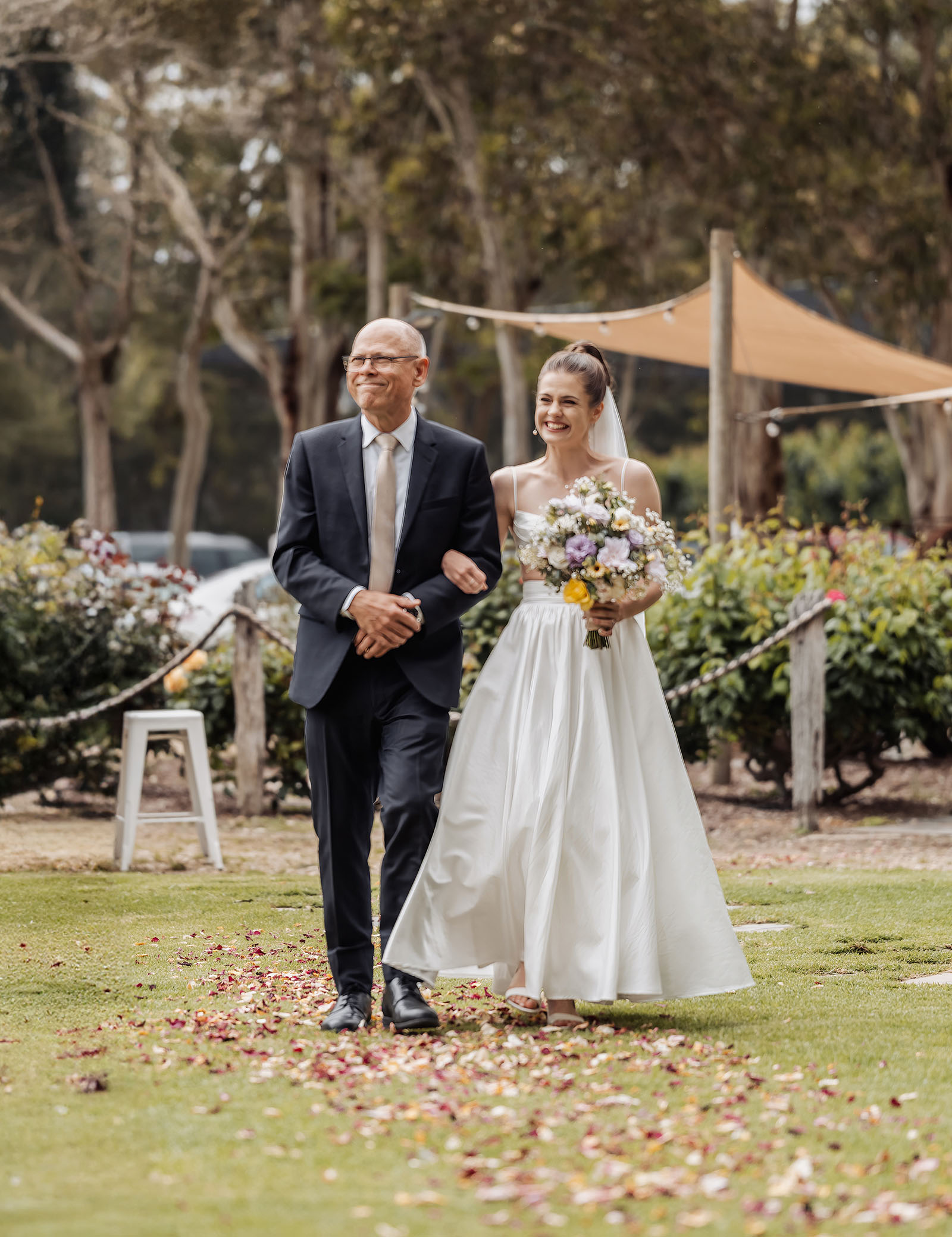 fleurieu cherries wedding - kimberley & richard 5 Bride walks with father down wedding aisle under blue sky.