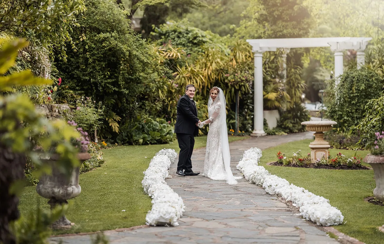 wedding at the manor in basket range - maryam & jason 153 Bride and groom walking down a garden path on their wedding day.