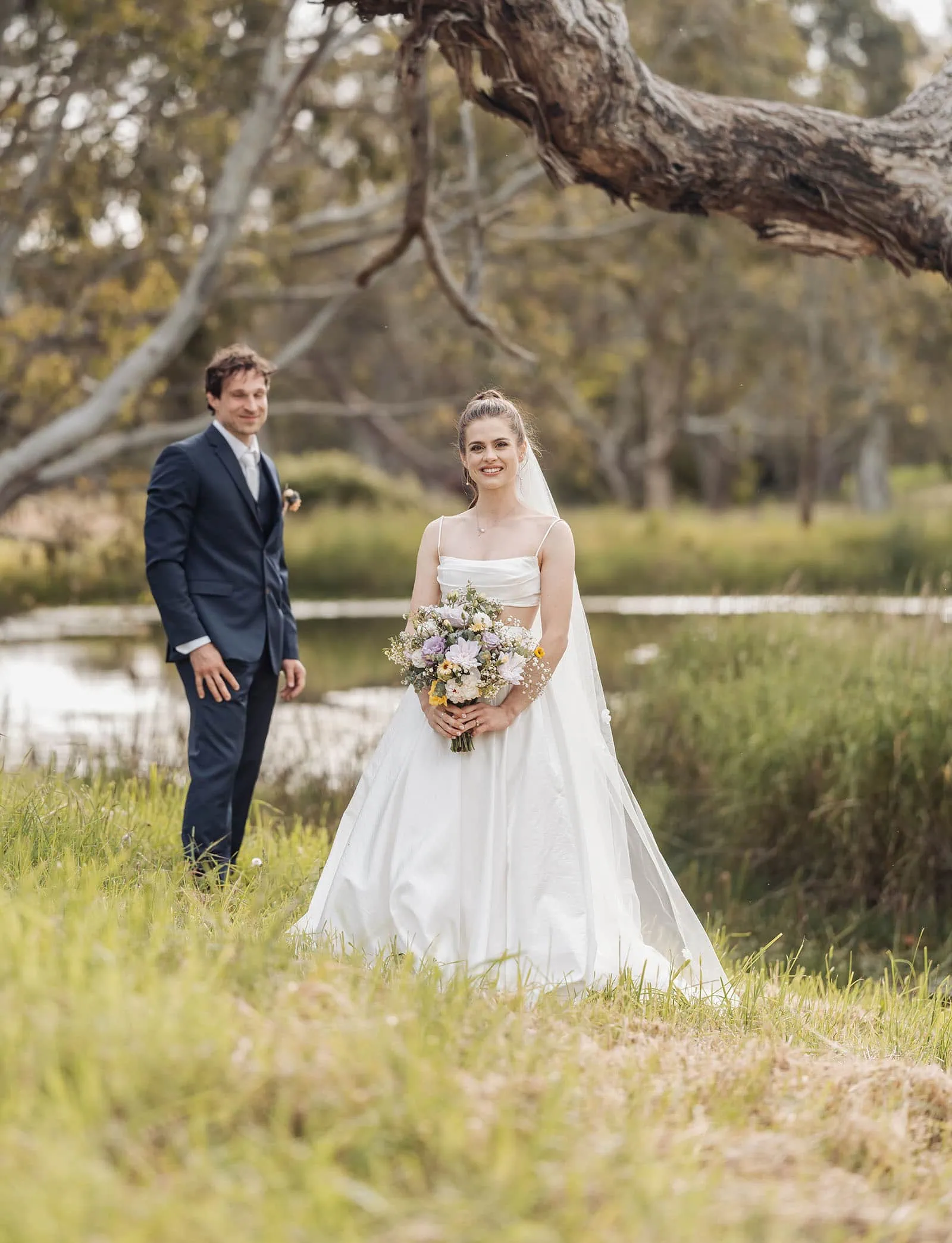 fleurieu cherries wedding - kimberley & richard 69 Bride and groom pose by a scenic river at an outdoor wedding ceremony.