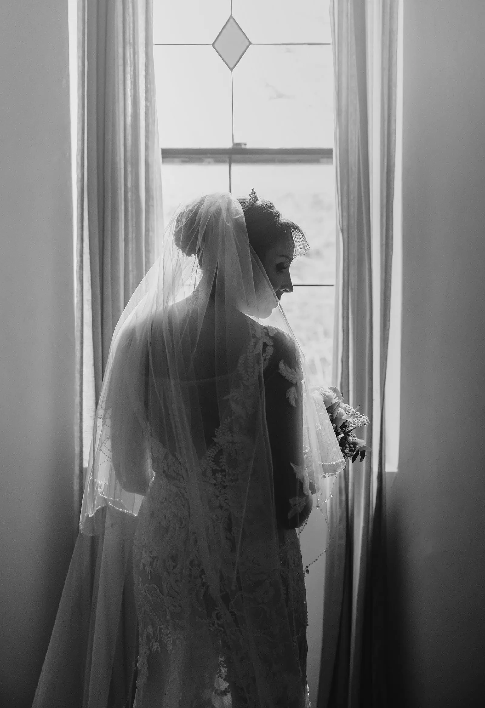 wedding at the manor in basket range - maryam & jason 128 Elegant bride gazing through window in portrait photo, wedding dress glowing in natural light.