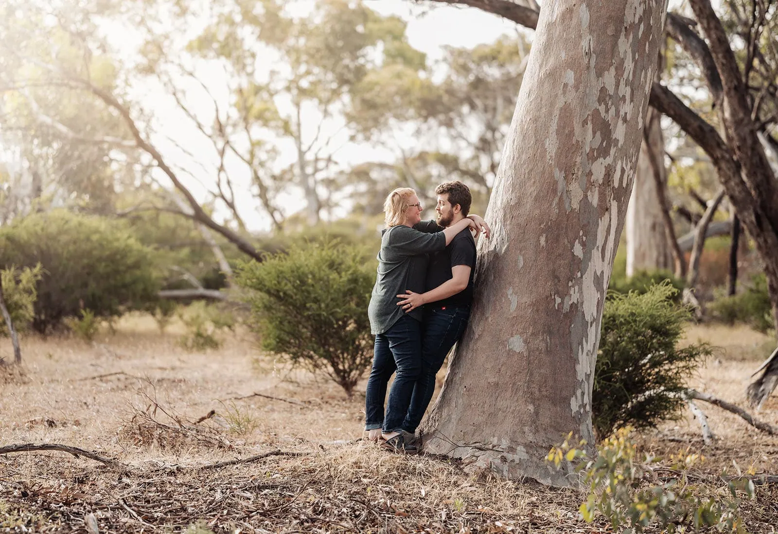 happy valley reservoir family shoot 87 Couple embraces near tree in serene woodland setting during golden hour.