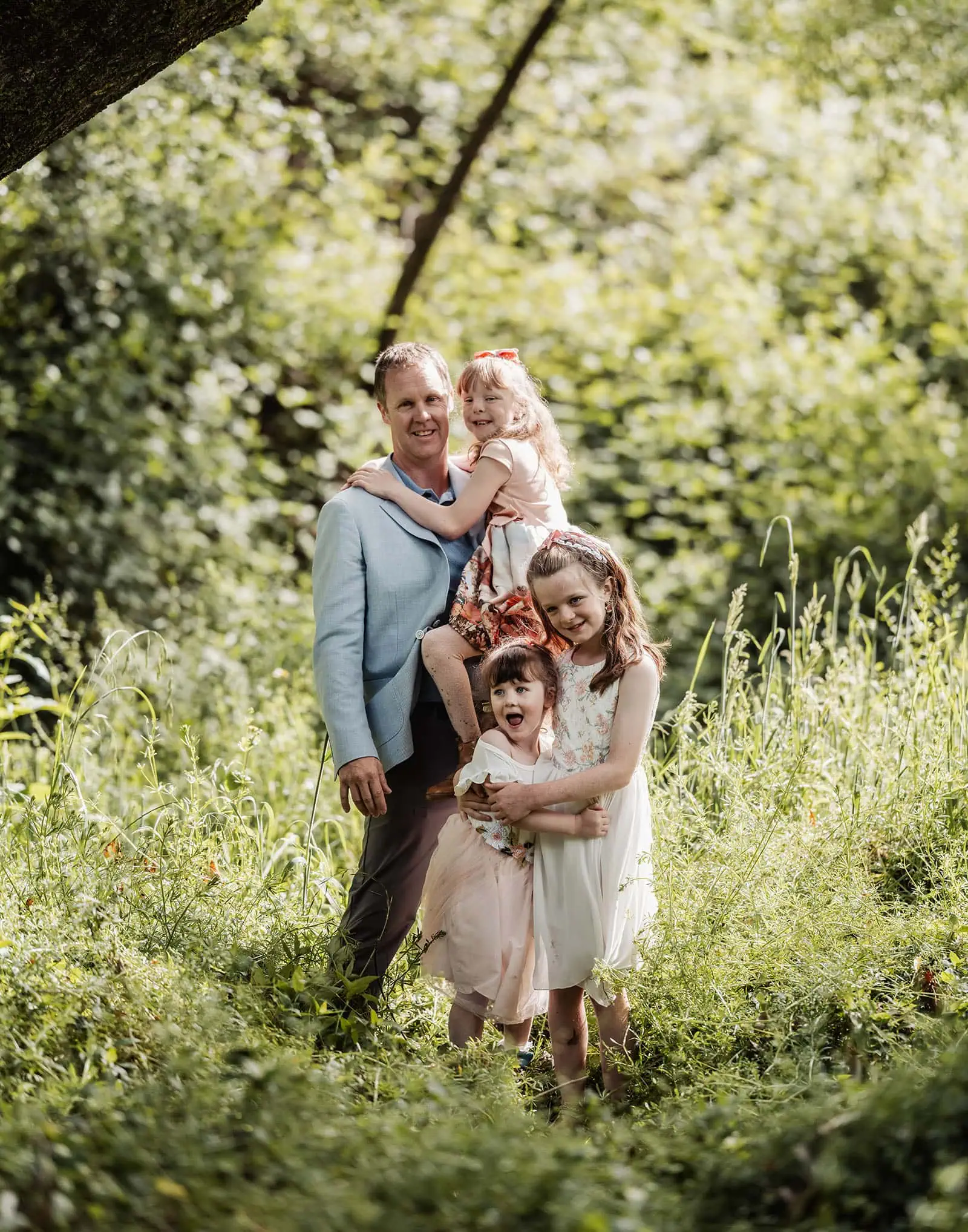 ironbank family photography 129 Family enjoying nature: man with children in floral dresses, surrounded by lush greenery.