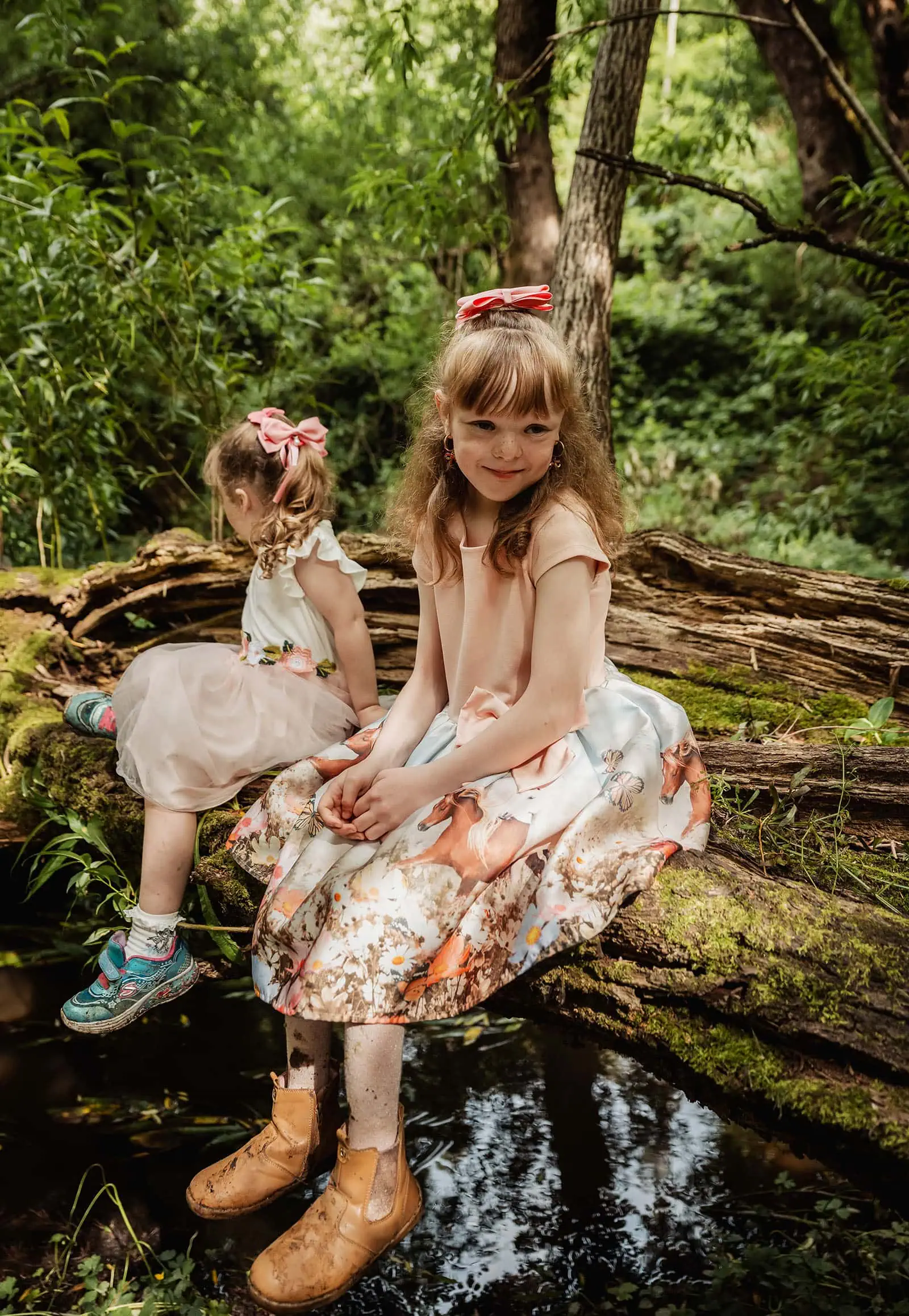ironbank family photography 122 Young girls sitting on fallen tree in lush forest, wearing pink dresses with bows.