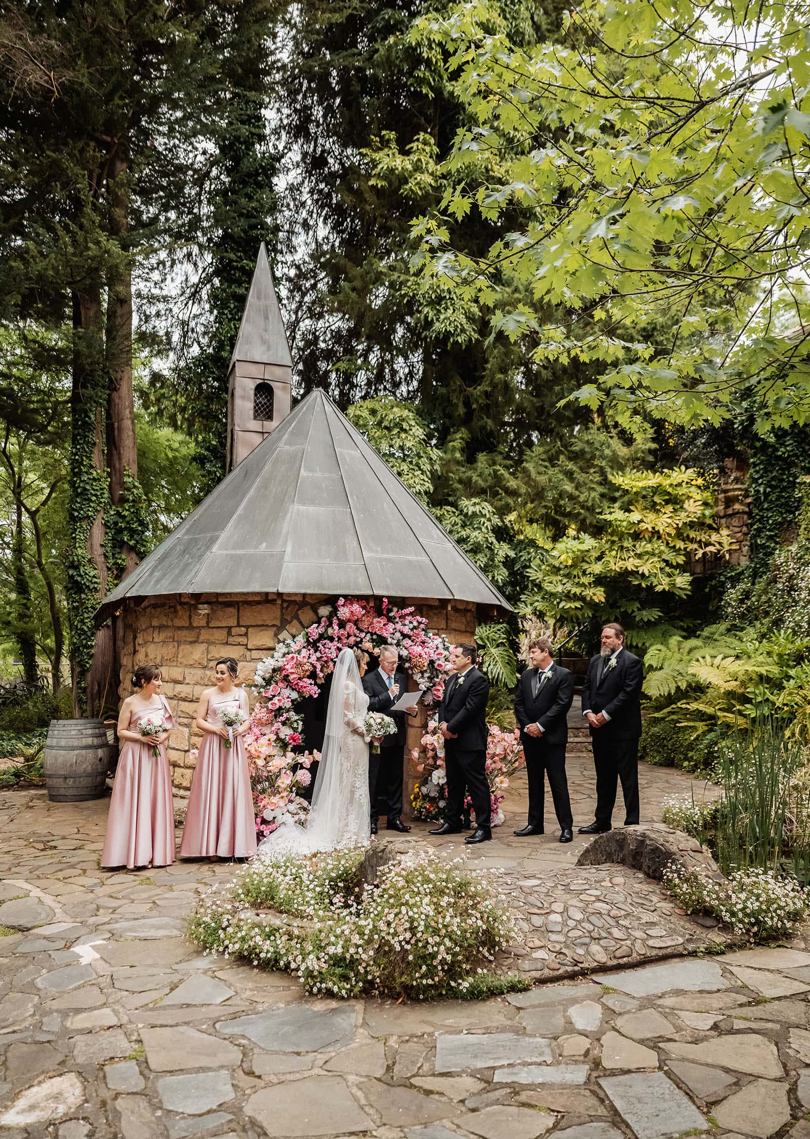wedding at the manor in basket range - maryam & jason 136 Elegant garden wedding ceremony with floral arches and guests.