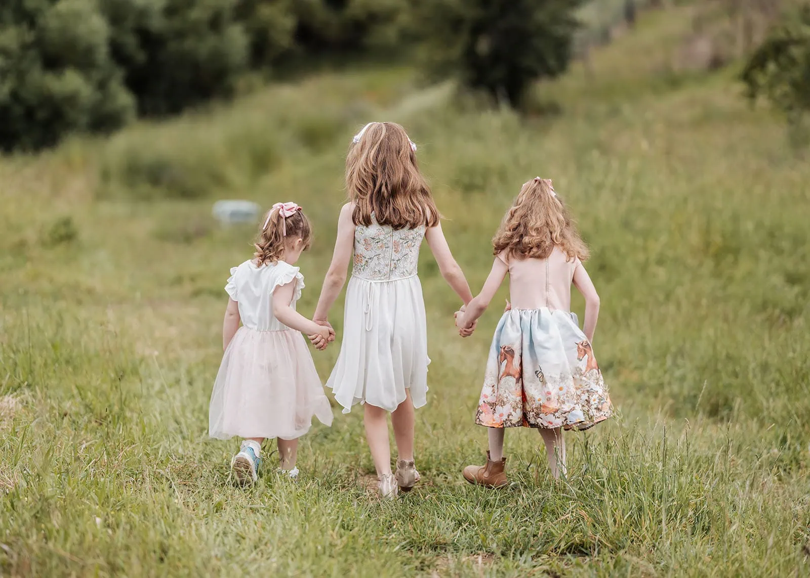 ironbank family photography 109 Three girls holding hands, exploring a lush meadow in elegant dresses.