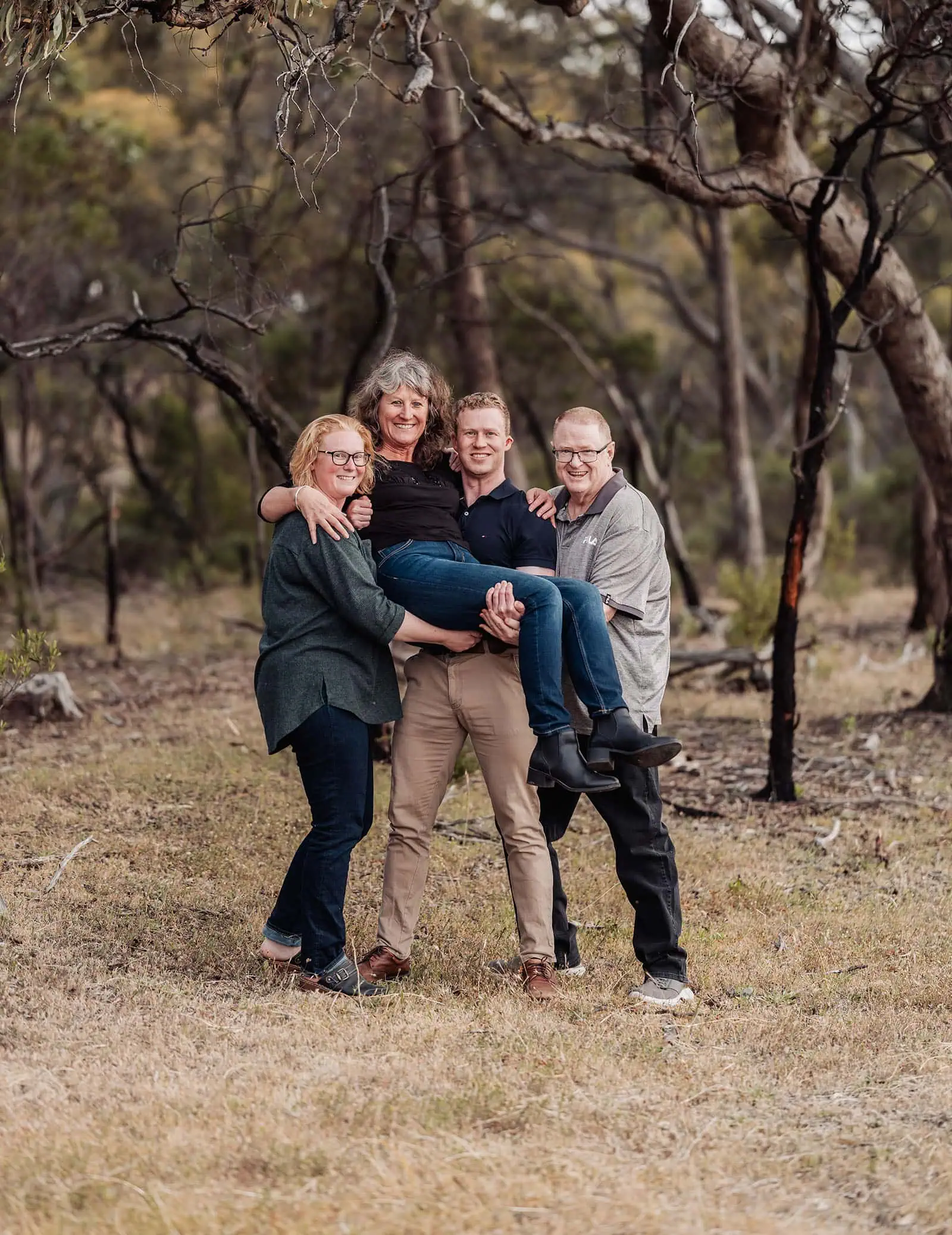 happy valley reservoir family shoot 107 Friends joyfully lifting a woman in an autumn woodland setting.