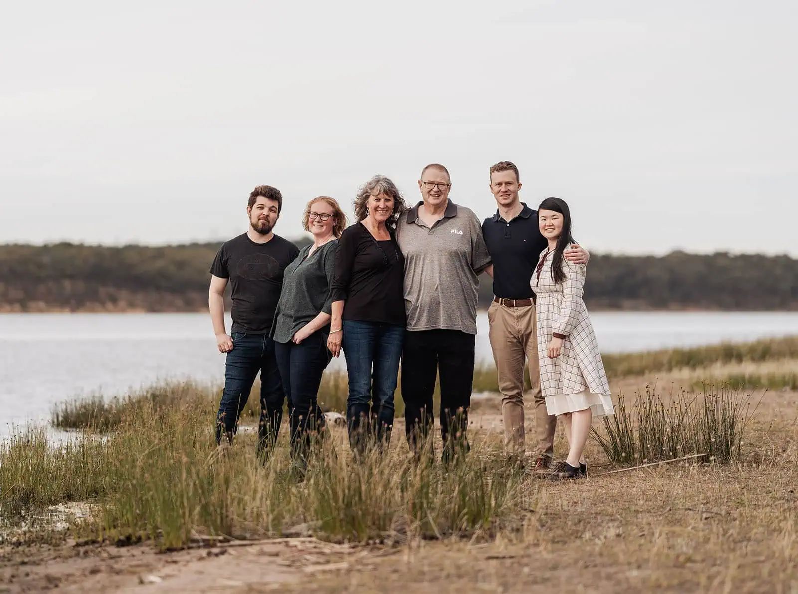 happy valley reservoir family shoot 104 Group of friends smiling by a scenic lakeside with trees in the background.