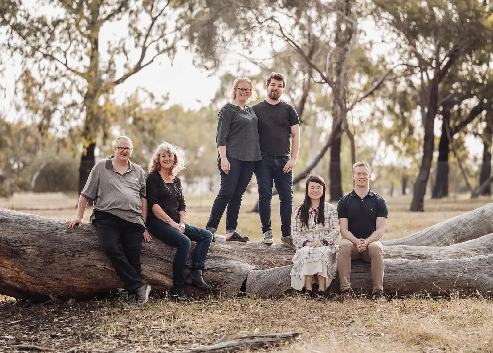 happy valley reservoir family shoot 84 Group of friends relaxing on a fallen tree in a serene wooded area.