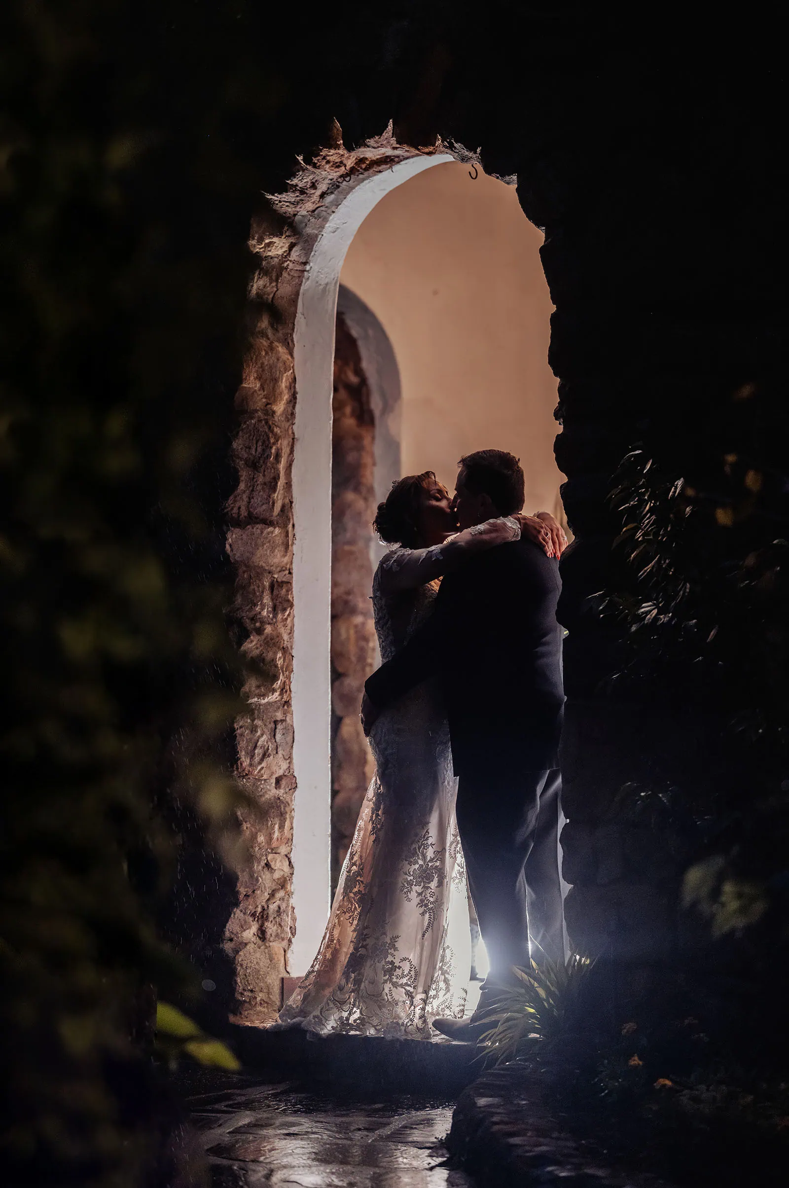 wedding at the manor in basket range - maryam & jason 162 Couple embraces under romantic stone archway at sunset.