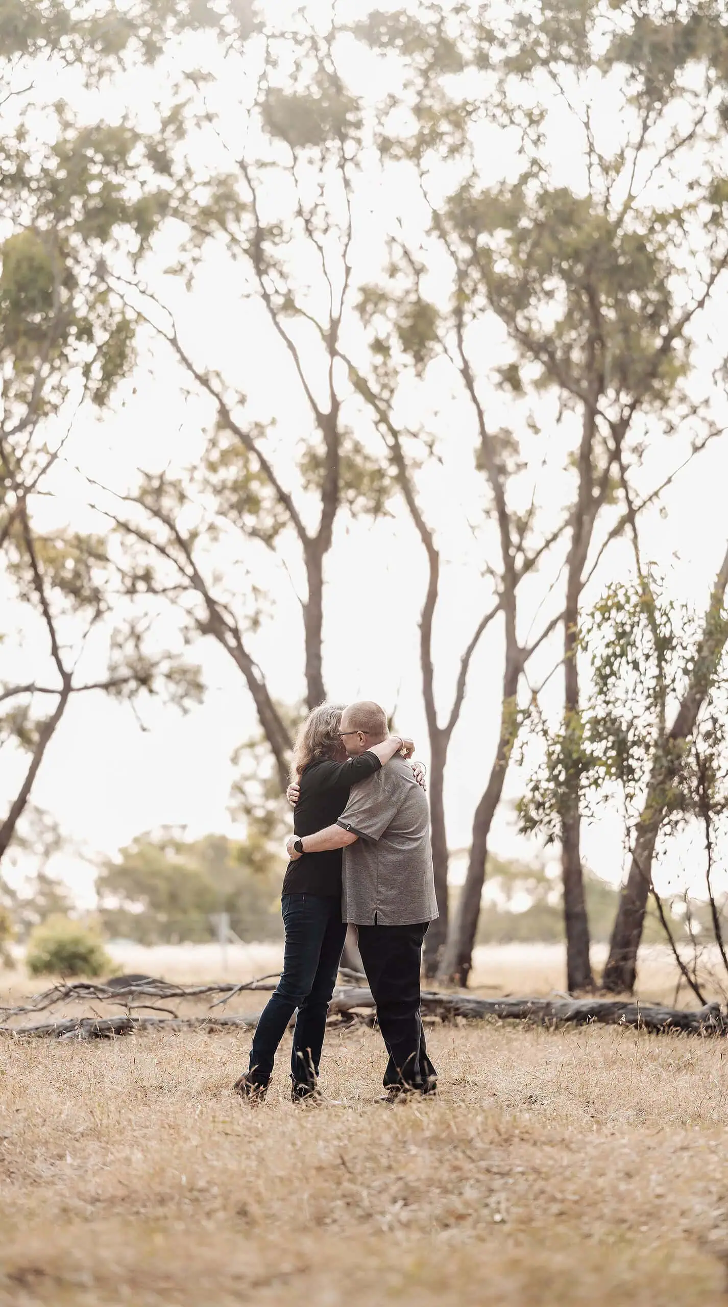 happy valley reservoir family shoot 90 Couple embracing in a serene field with golden grass and tall trees in late summer light.
