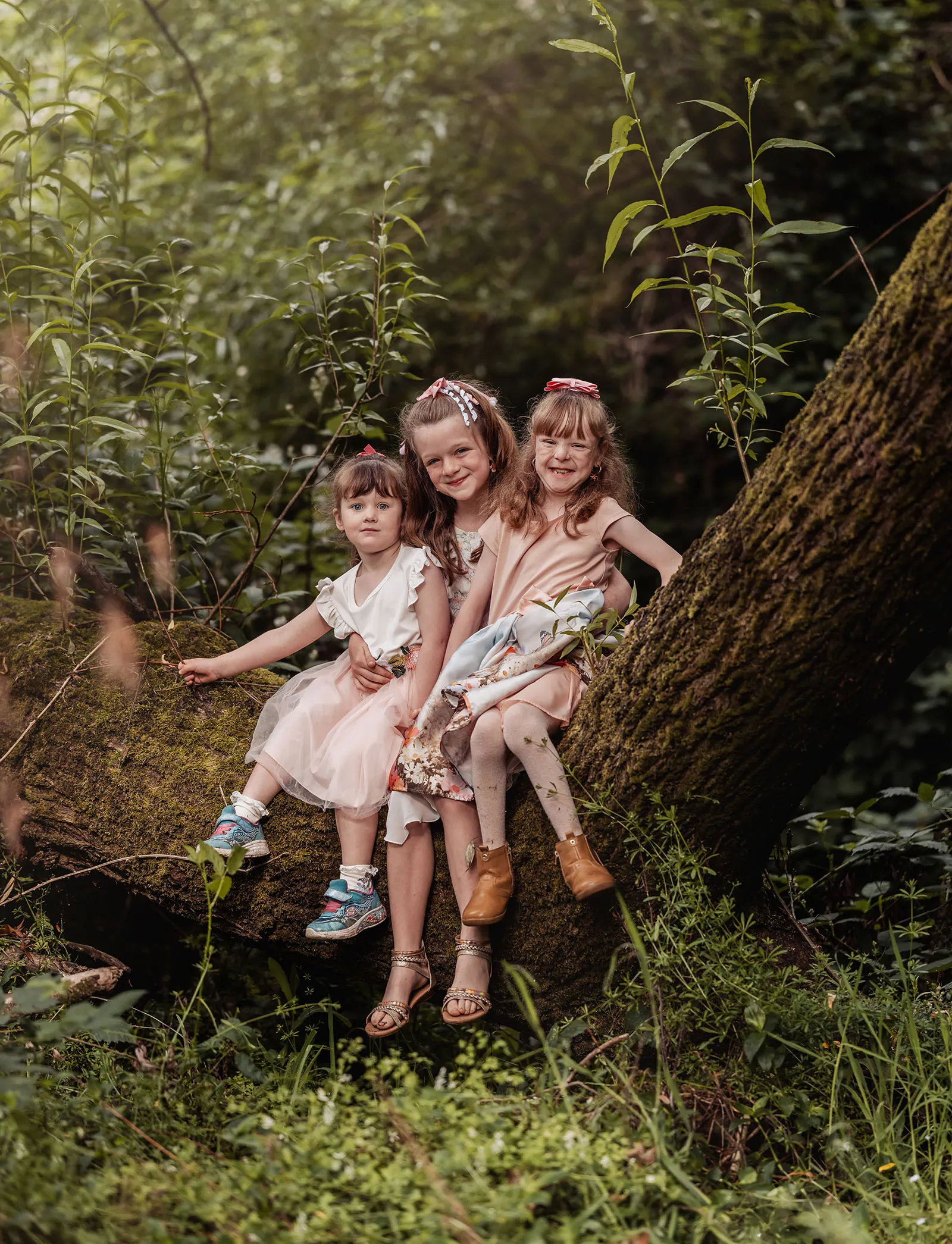 ironbank family photography 113 Three girls sit on a mossy tree branch in a lush forest, enjoying nature.