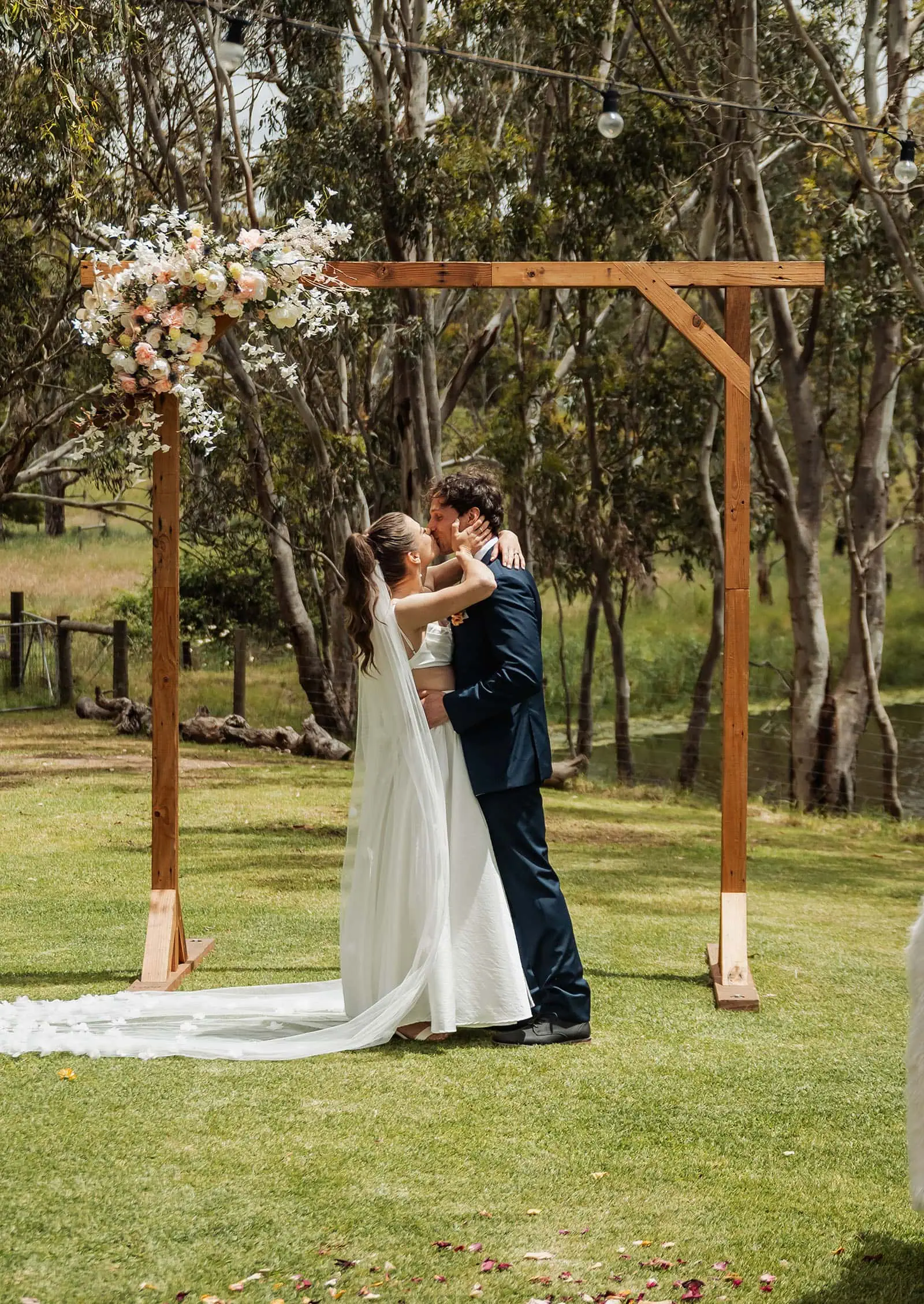 fleurieu cherries wedding - kimberley & richard 20 Bride and groom kiss under floral wedding arch outdoors.