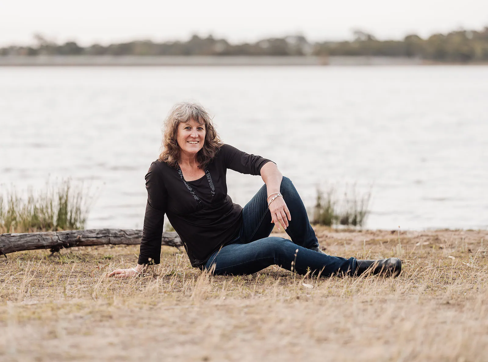 happy valley reservoir family shoot 101 Woman relaxing by a tranquil lakeside, wearing casual attire amidst serene natural surroundings.