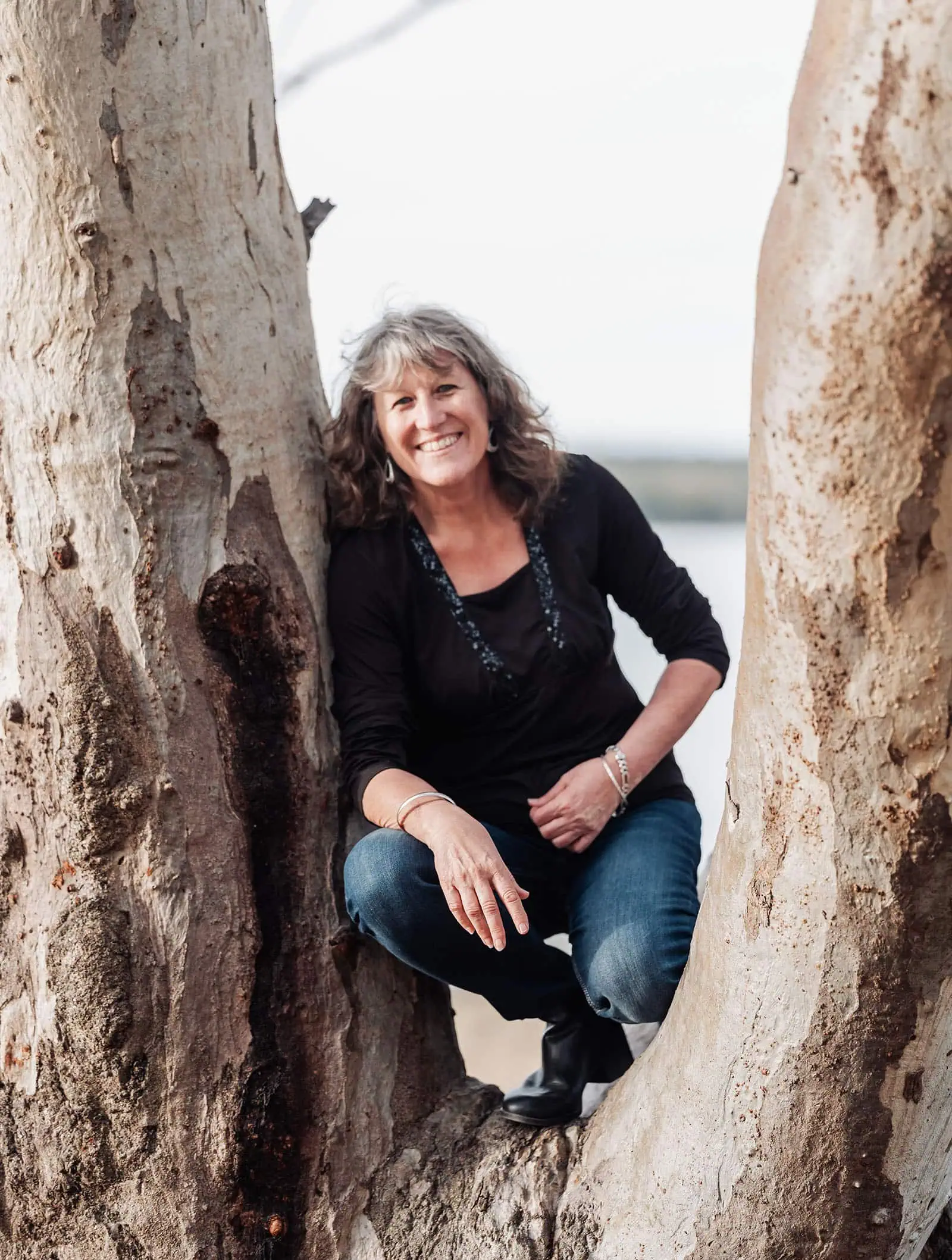 happy valley reservoir family shoot 92 Woman smiling between tree trunks in natural setting.