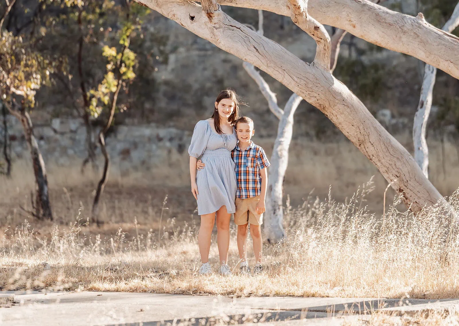 beautiful anstey hill family photoshoot 18 Smiling woman and boy in sunlit park, surrounded by eucalyptus trees and dry grass.
