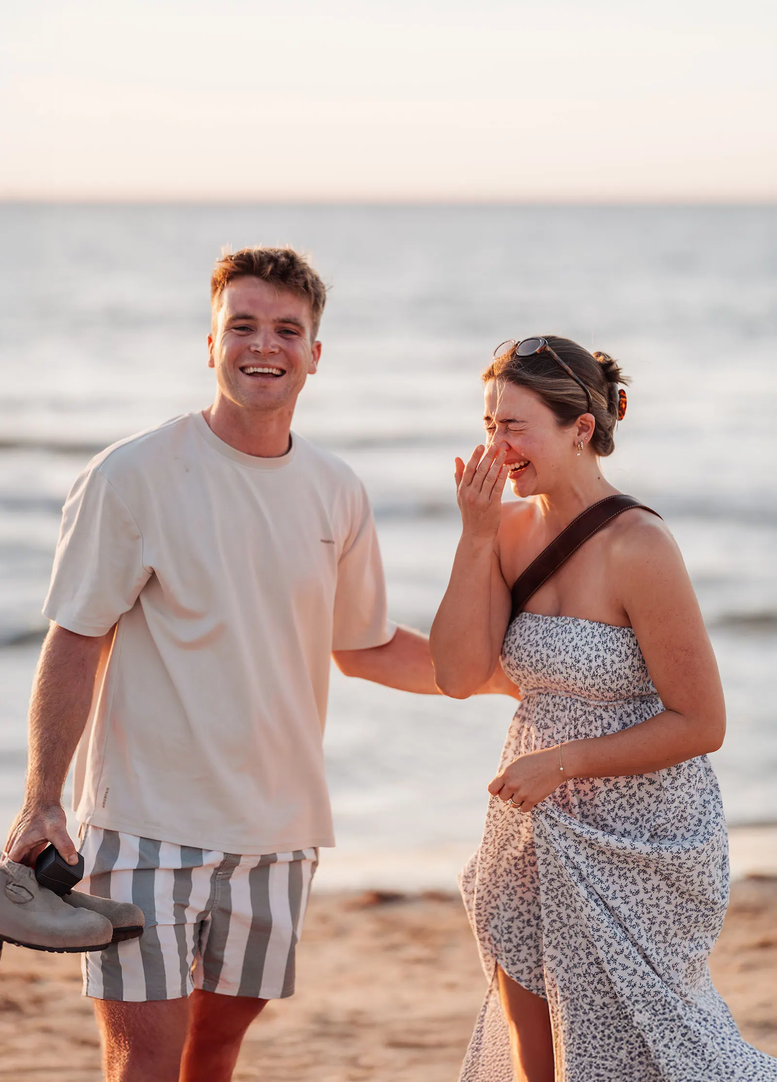 christies beach proposal – hollie & william 37 Couple enjoying sunset on beach, barefoot, with ocean waves and serene skyline.
