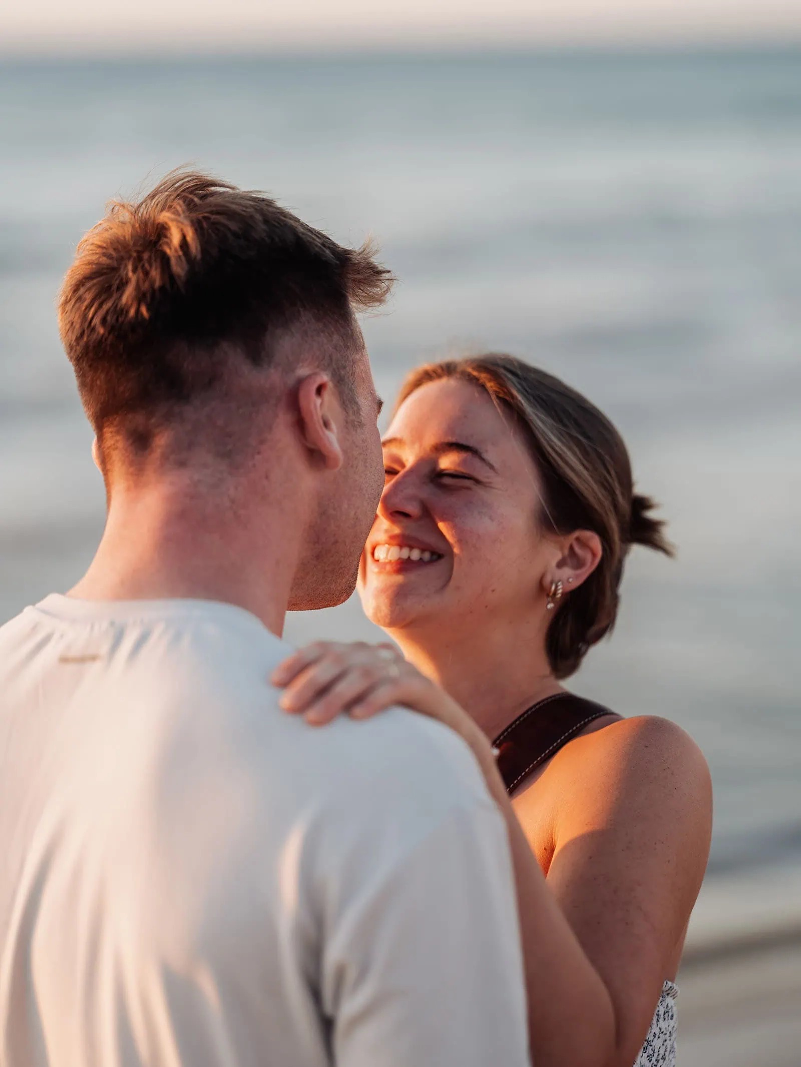 christies beach proposal – hollie & william 44 Couple embraces on serene beach at sunset, highlighting engagement and intimate, joyful moment.