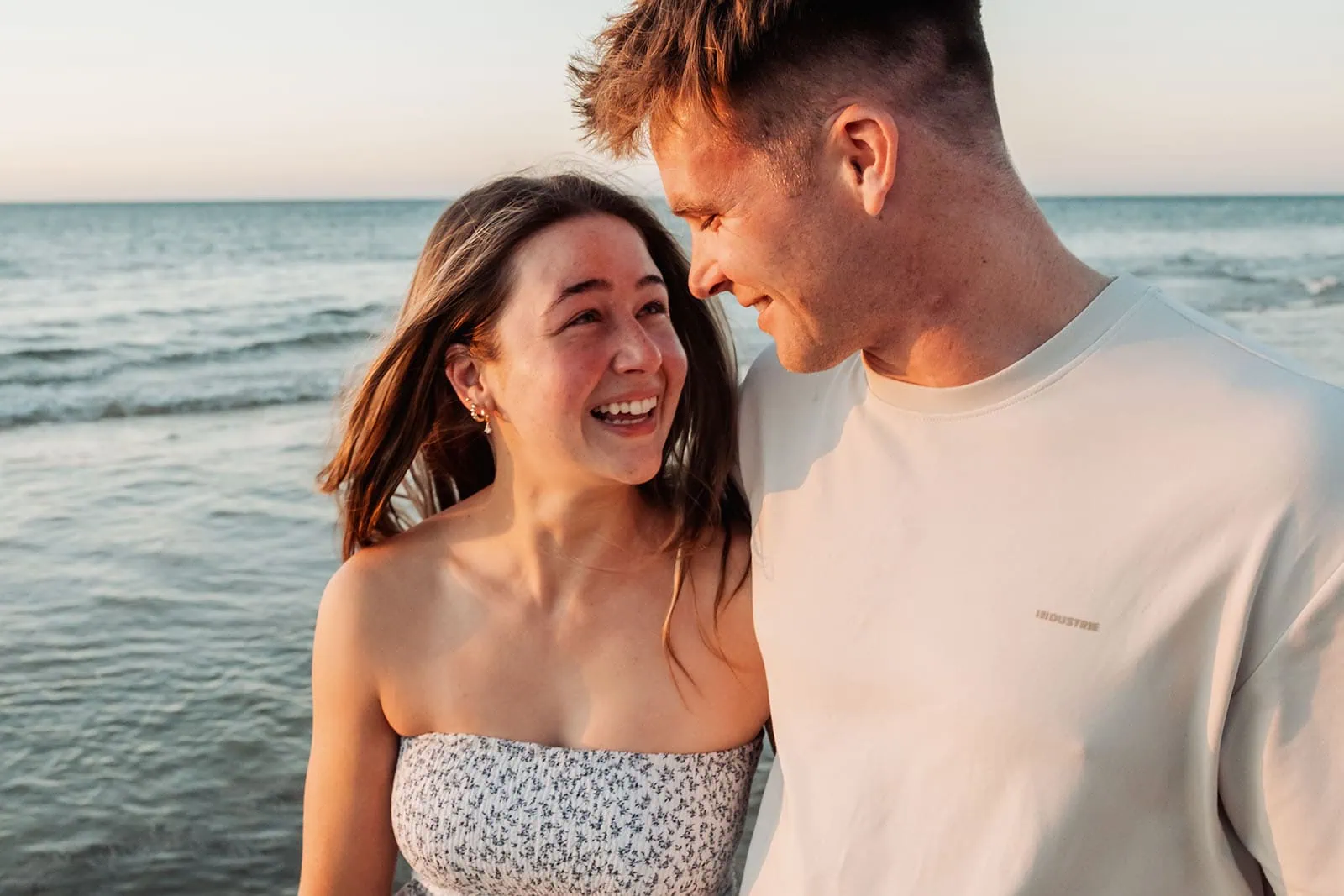 christies beach proposal – hollie & william 45 Couple smiling at sunset on beach with ocean backdrop.