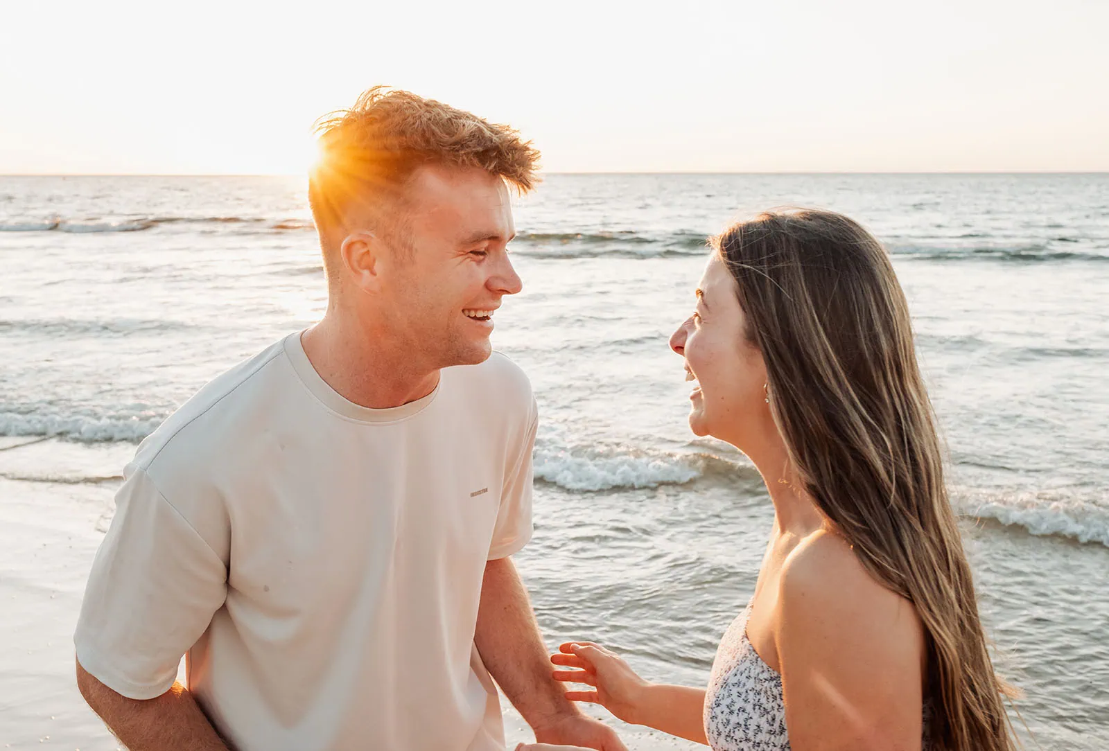 christies beach proposal – hollie & william 41 Couple laughing on beach at sunset with ocean waves in background.
