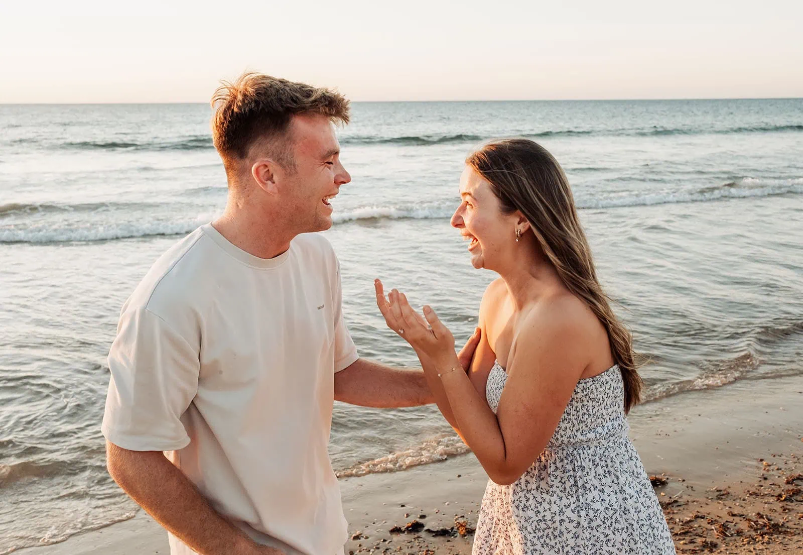 christies beach proposal – hollie & william 39 Couple laughing on beach at sunset, enjoying carefree moment by ocean waves.