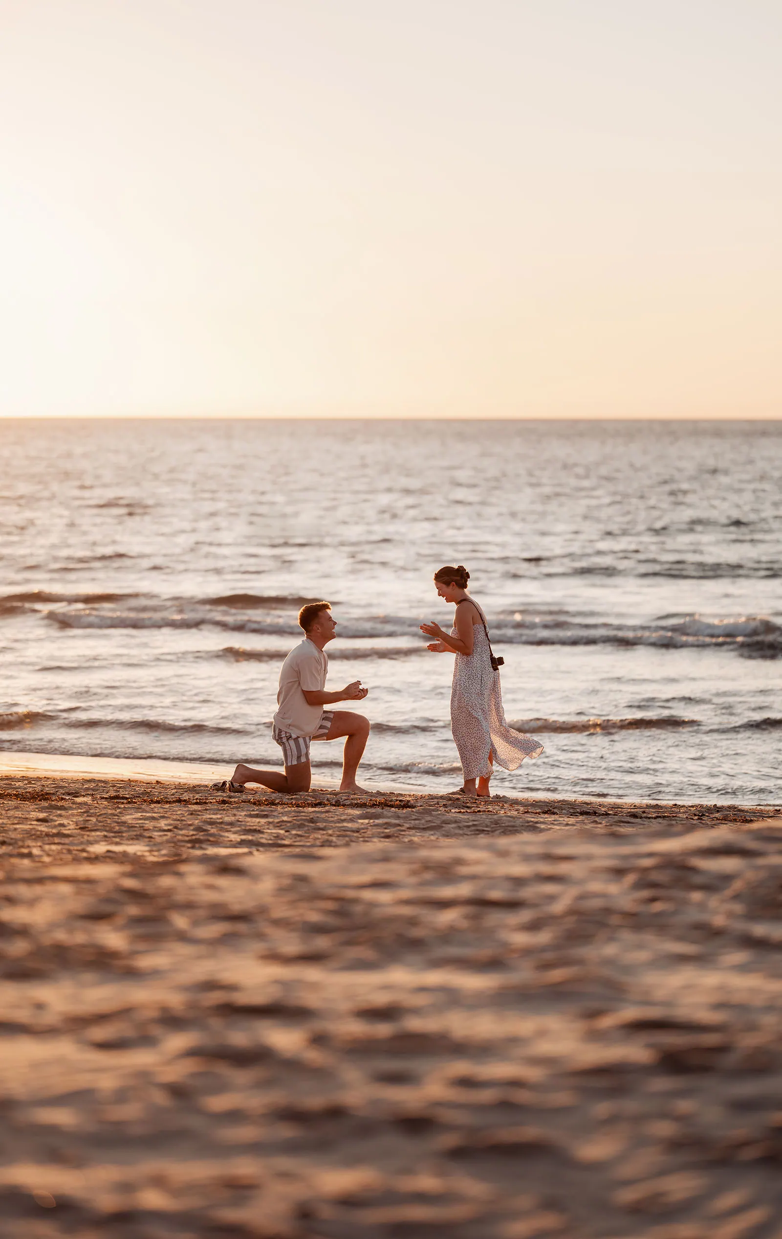 christies beach proposal – hollie & william 32 Beach proposal at sunset with man kneeling, offering ring to surprised woman.
