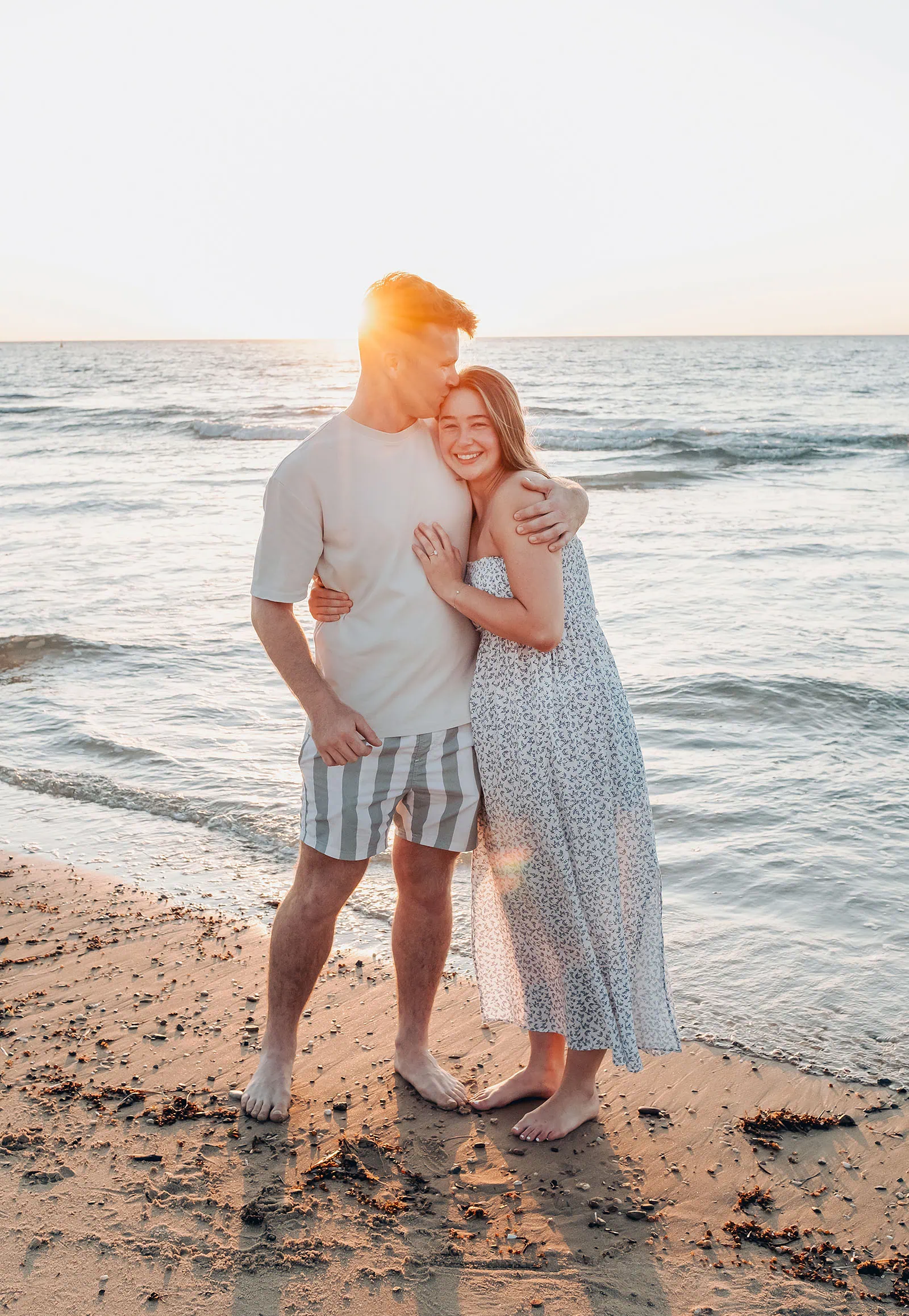 christies beach proposal – hollie & william 42 Couple embracing on sunset beach, ocean waves, romantic moment.