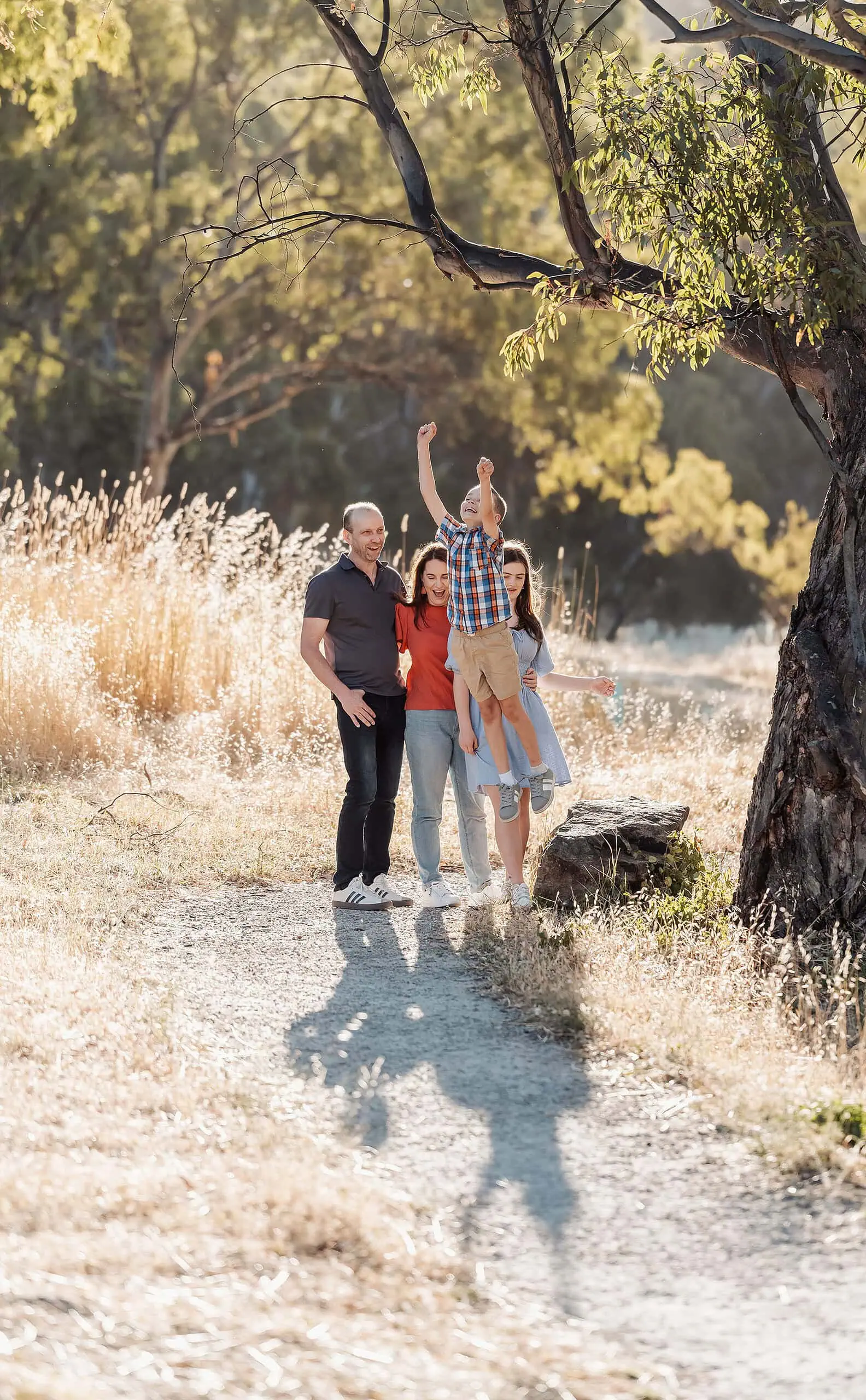 beautiful anstey hill family photoshoot 25 Family enjoying nature together on a sunny path, with joyful child lifted in celebration.