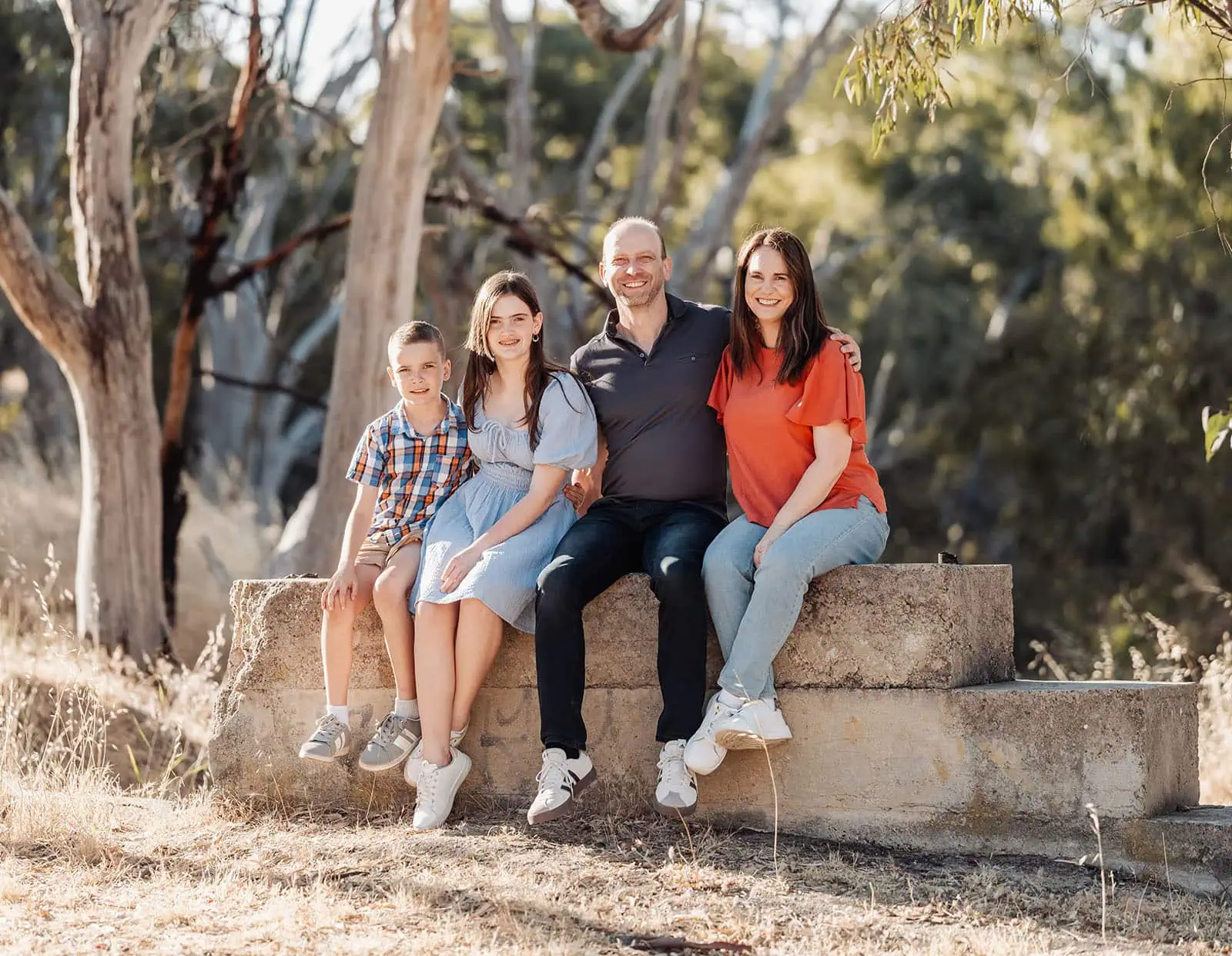 beautiful anstey hill family photoshoot 15 Family enjoying a sunny day in nature, seated on a rustic bench.