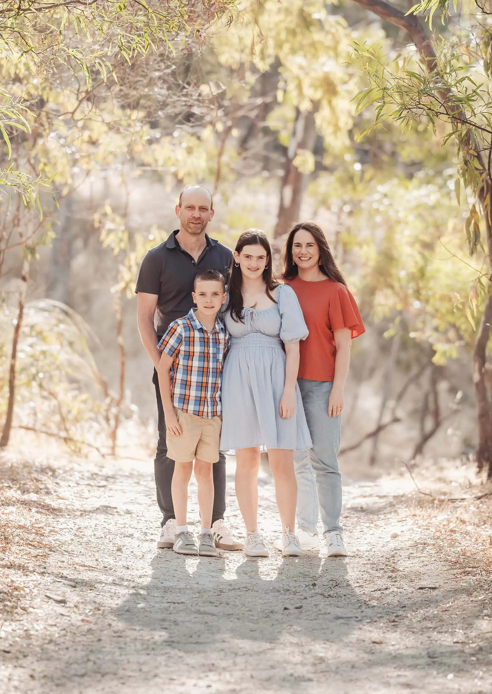 beautiful anstey hill family photoshoot 8 Family walking in forest, smiling under sunlight, casual attire, nature background.
