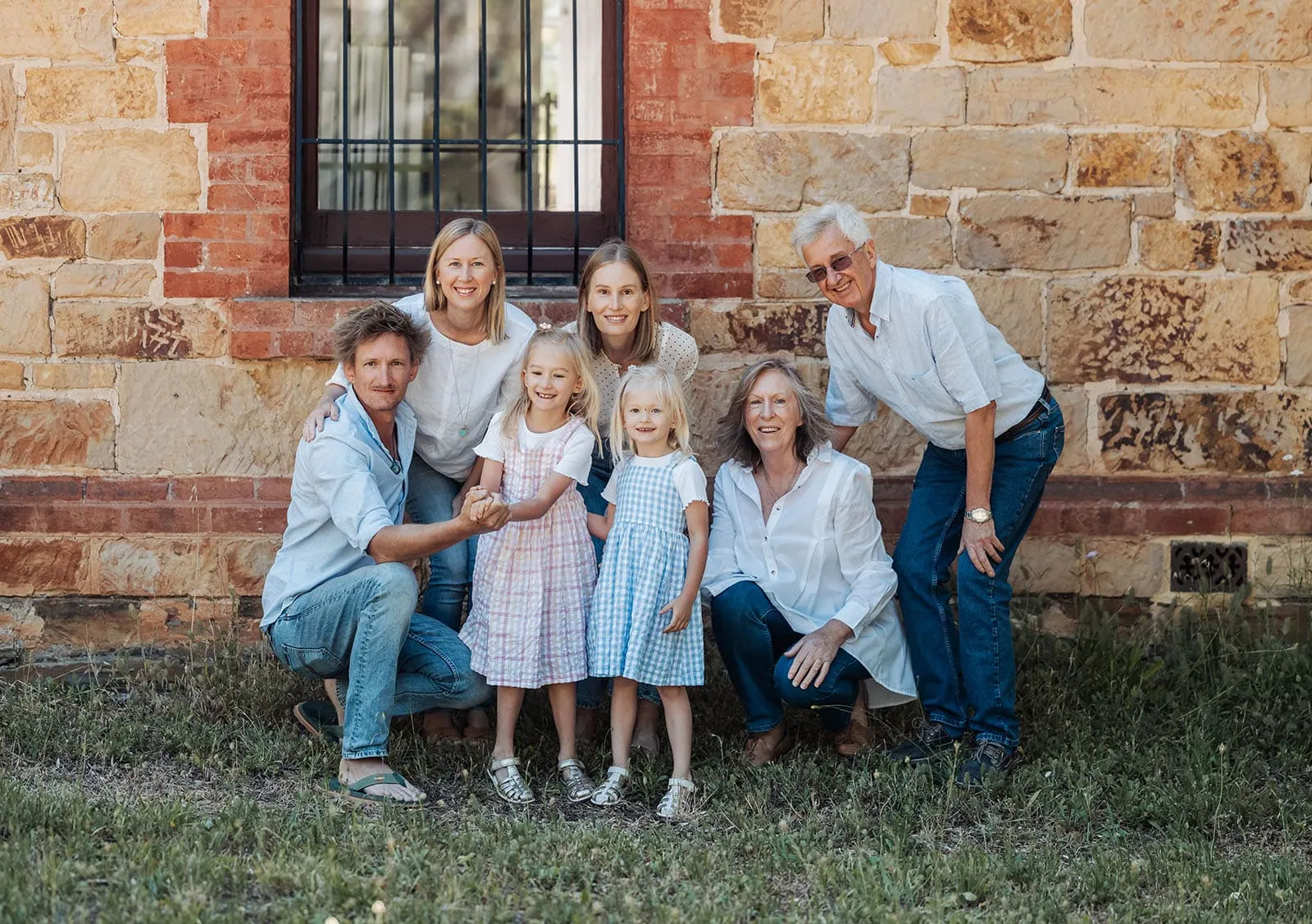 blackwood forest family photography 68 Multi-generational family outdoors by rustic stone wall, wearing casual outfits, expressing joy.