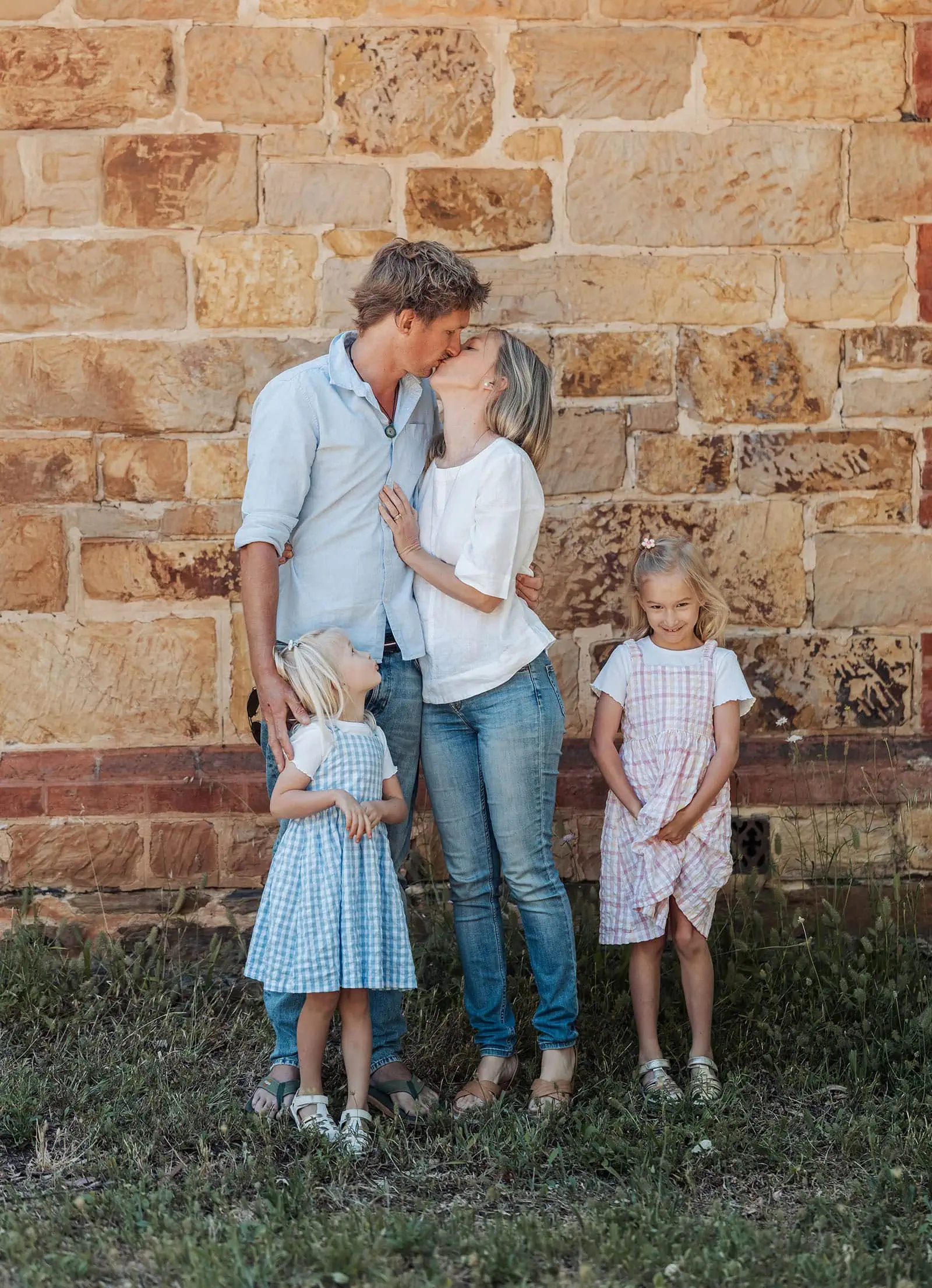 blackwood forest family photography 69 Family sharing affectionate moment by rustic brick wall with daughters in gingham dresses.